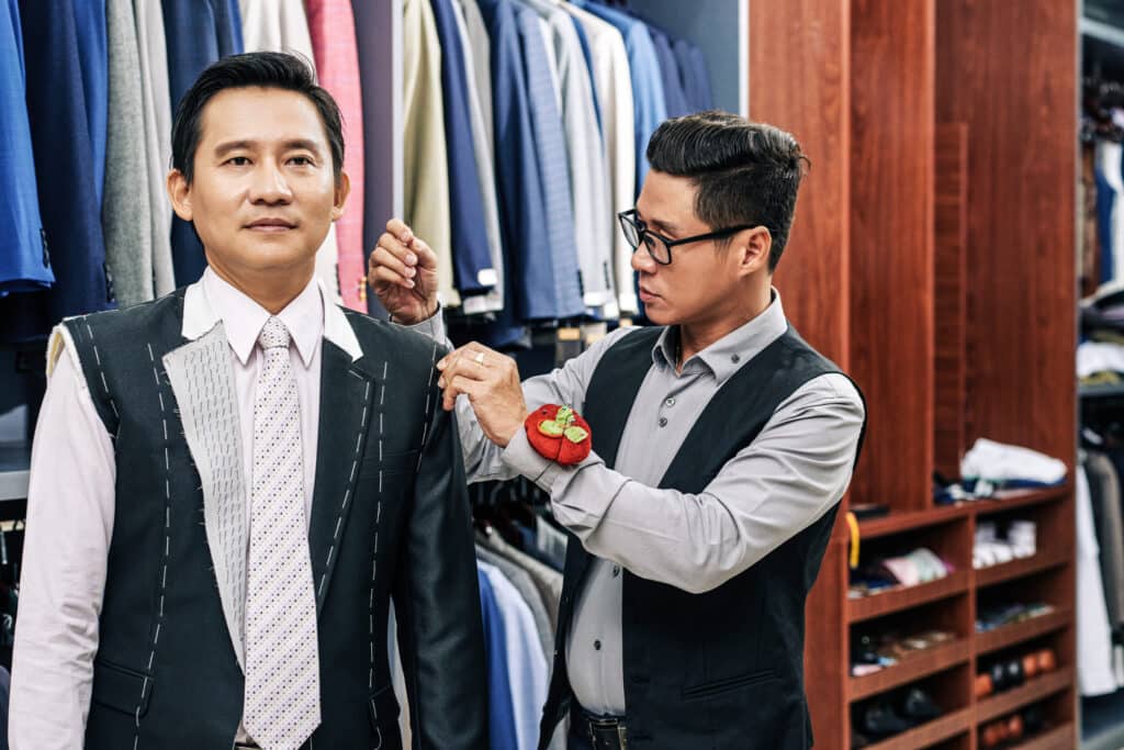 Custom tailor pinning shoulder during basted fitting for client