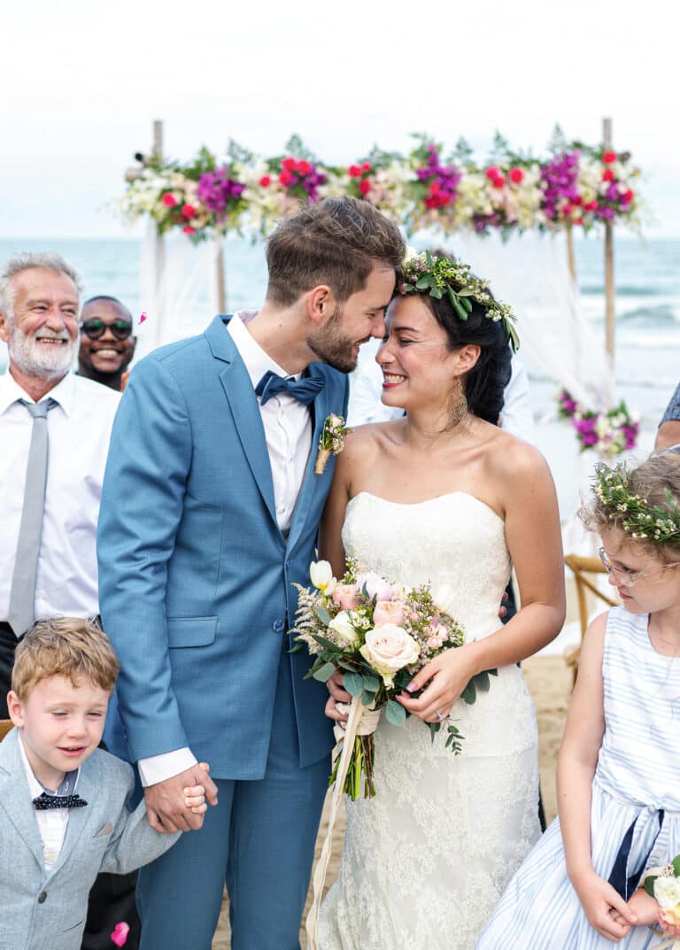 Bride and groom on beach holding hands. Groom in postman blue Zegna custom suit, bride in low cut wedding dress.
