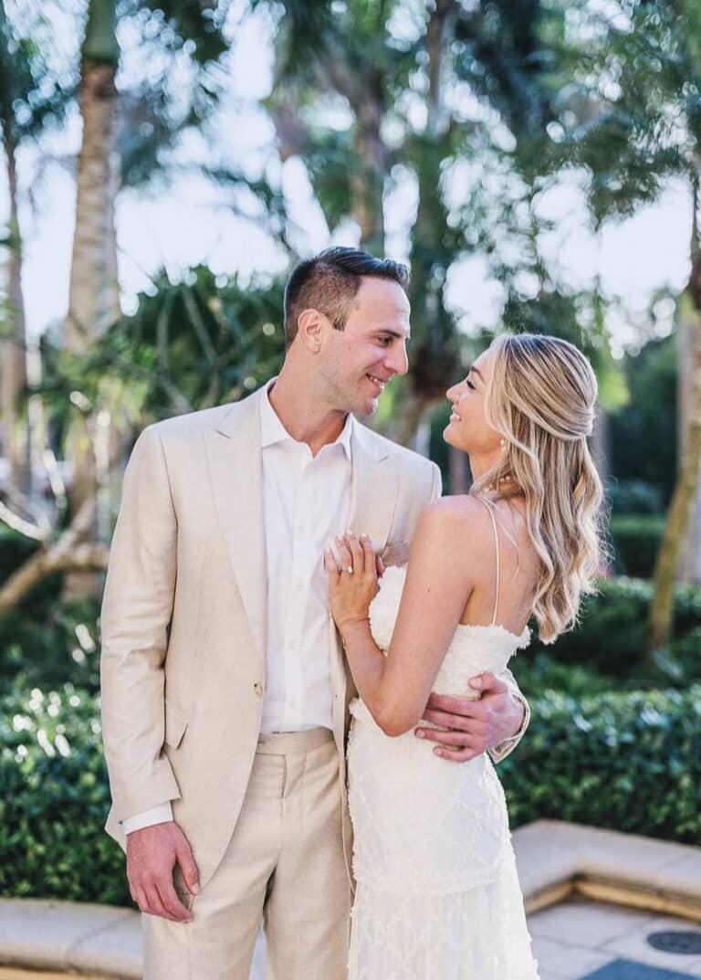 Groom and bride on beach looking at each other. Groom in off white custom made linen suit, bride in wedding dress.