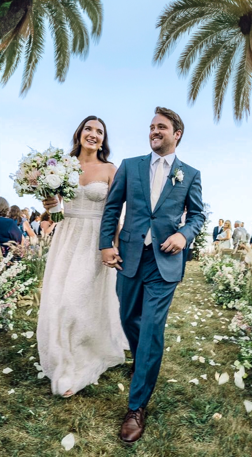 Bride and groom on beach holding hands. Groom in postman blue Zegna custom suit, bride in low cut wedding dress.