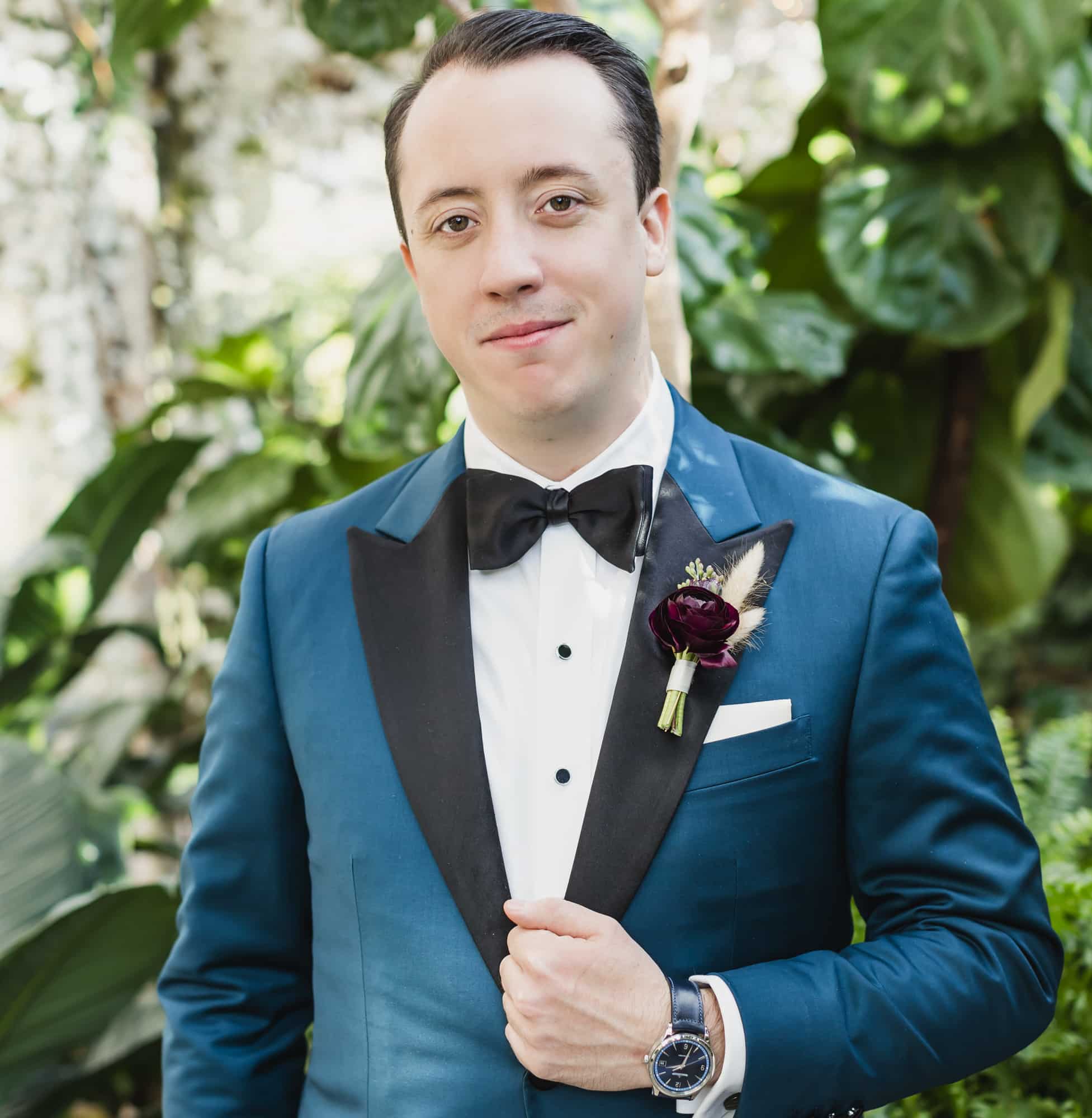 Groom outdoors wearing blue wedding custom tailored tuxedo with black peak lapel. Fabric by Scabal.