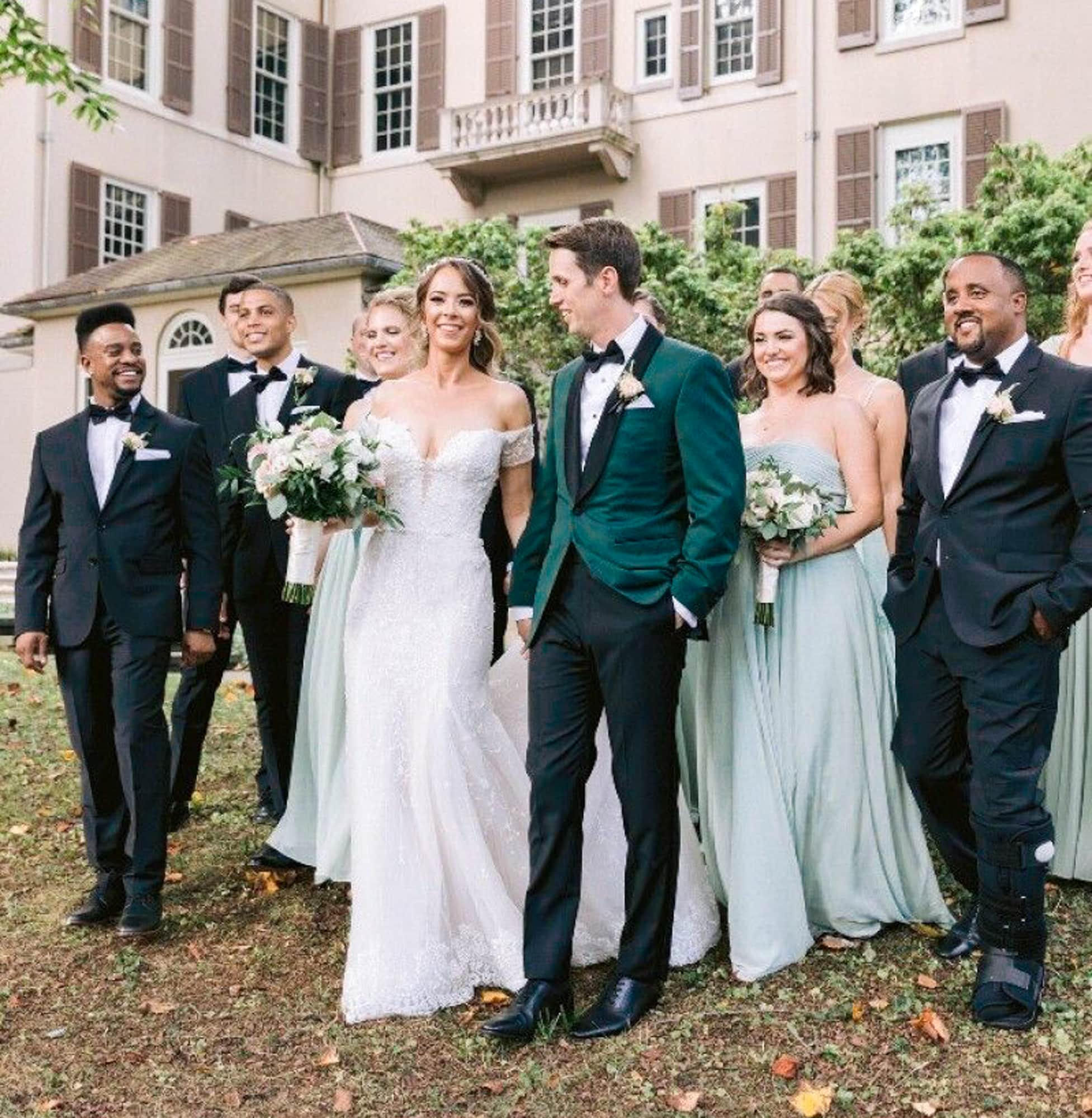 Bride and groom walking with guests. Groom wearing green bespoke wedding dinner jacket with black satin shawl lapel. Bride in wedding dress.