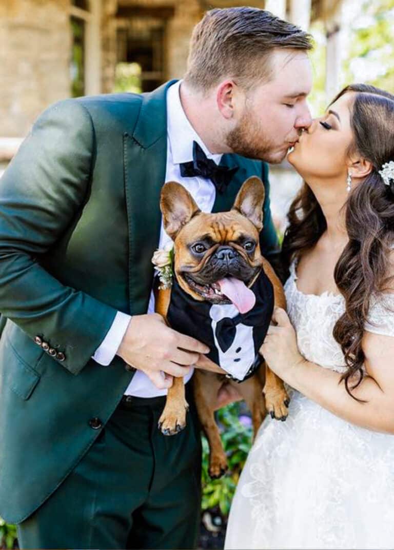 Bride and groom kissing. Groom wearing dark green bespoke suit with white shirt and black bowtie. Fabric by Scabal. Bride in low cut wedding dress.