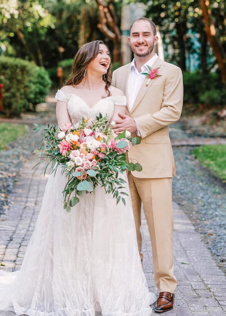 Bride and groom outdoors. Groom wearing Loro Piana linen off-white custom suit with open collared off white shirt. Bride in long wedding gown.
