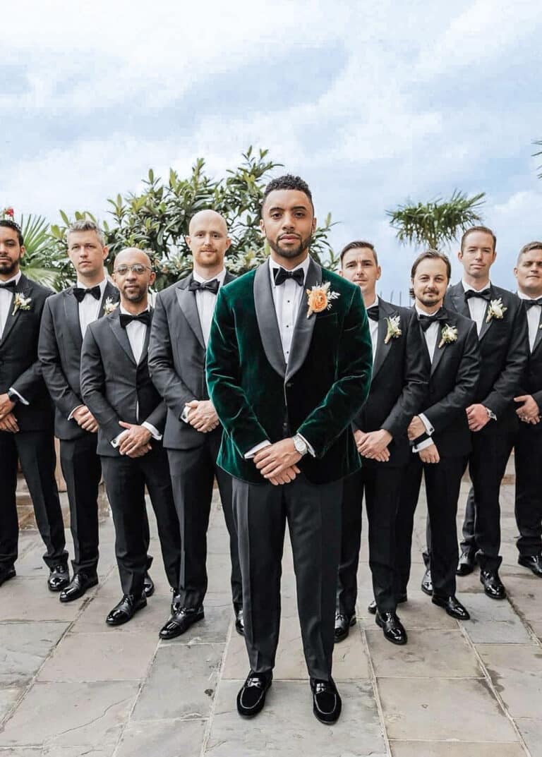 Groom standing with 8 groomsmen. Groom wearing custom made green velvet dinner jacket with green shawl lapel and black bowtie.