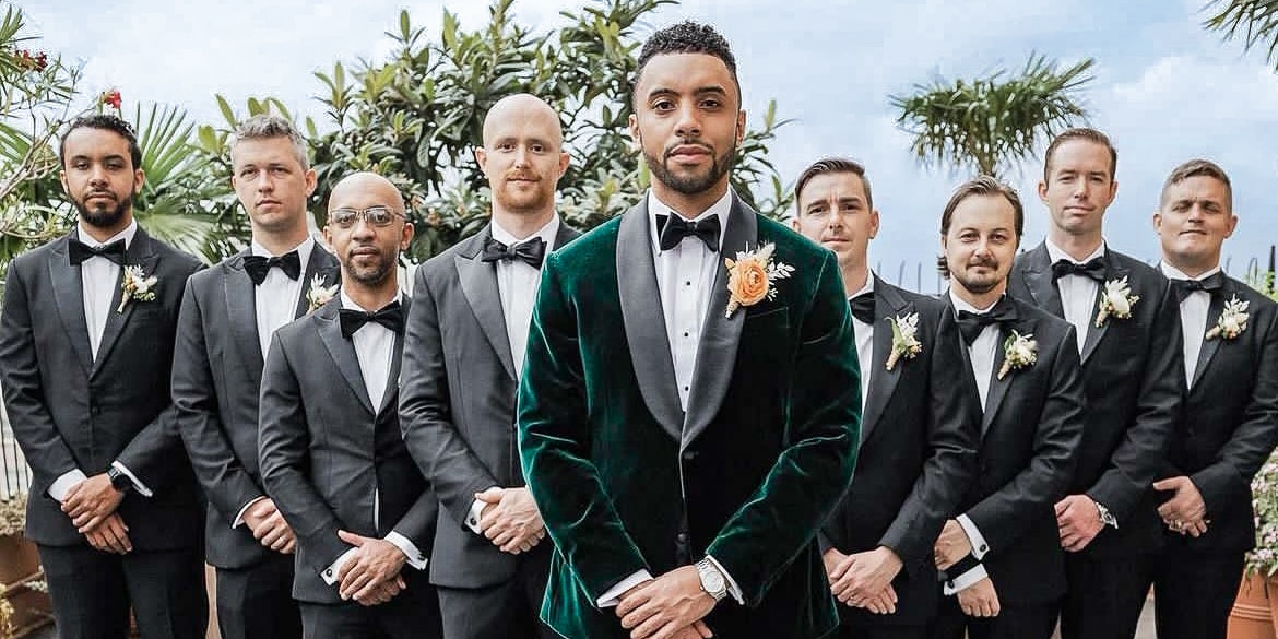 Groom standing with 8 groomsmen. Groom wearing custom made green velvet dinner jacket with green shawl lapel and black bowtie.