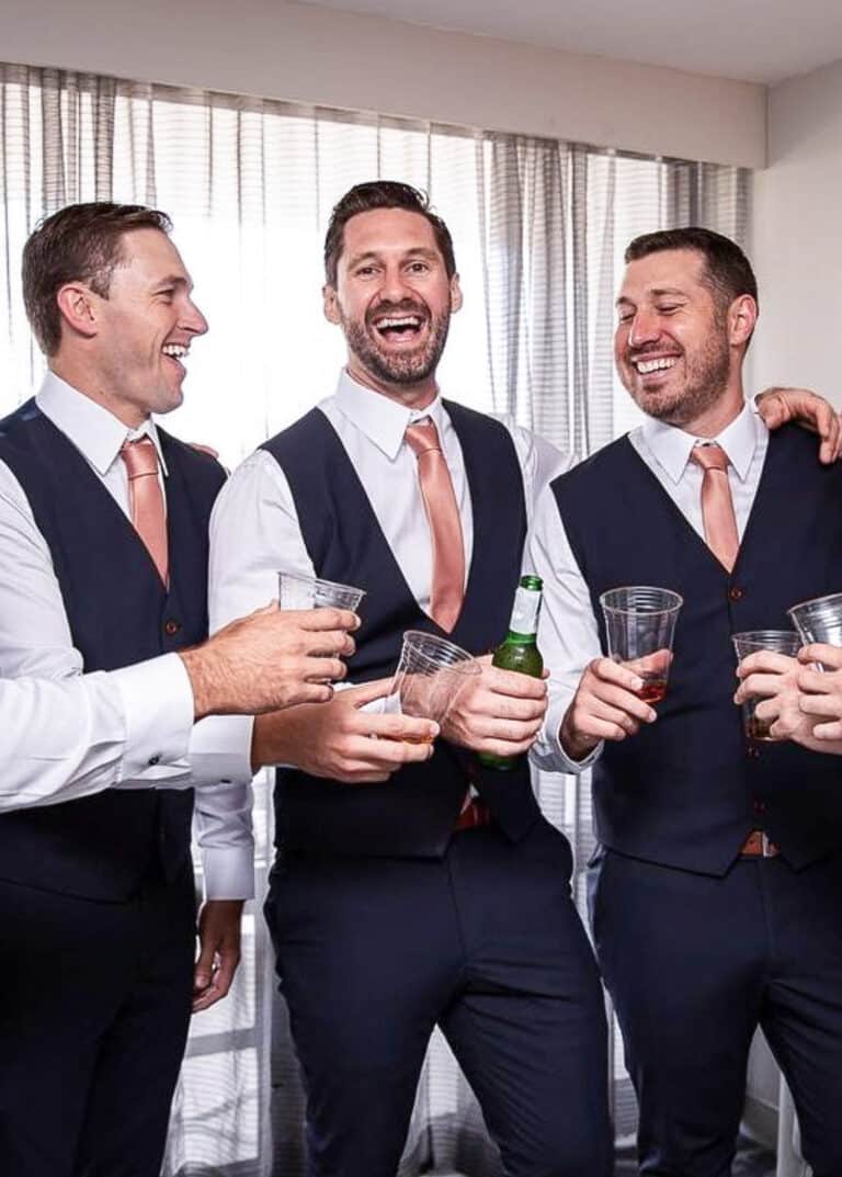 Four groomsmen all in matching navy vests and matching orange ties.