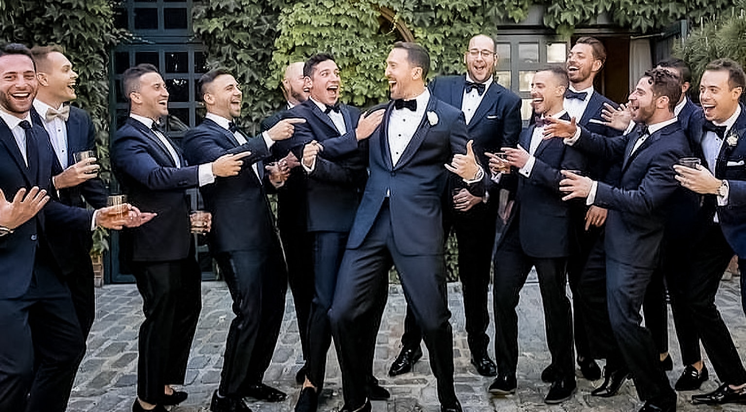 Groom taking picture with many groomsmen. Groom in bespoke blue suit.