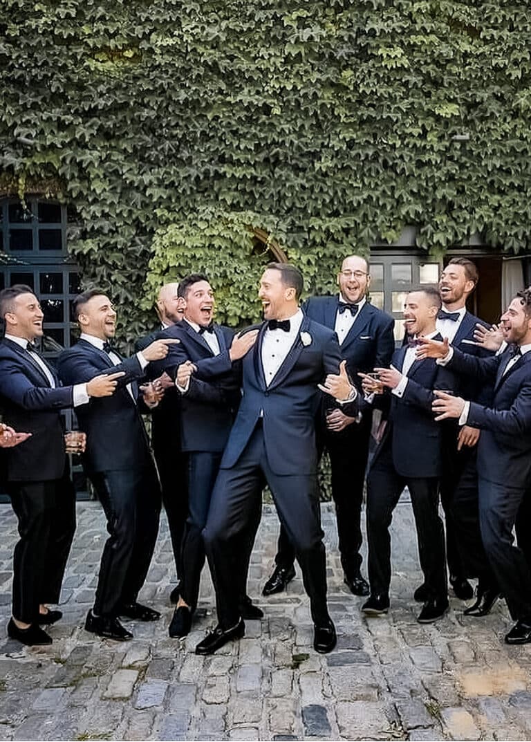 Groom taking picture with many groomsmen. Groom in bespoke blue suit.