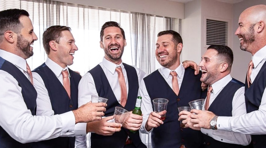 Four groomsmen all in matching navy vests and matching orange ties.