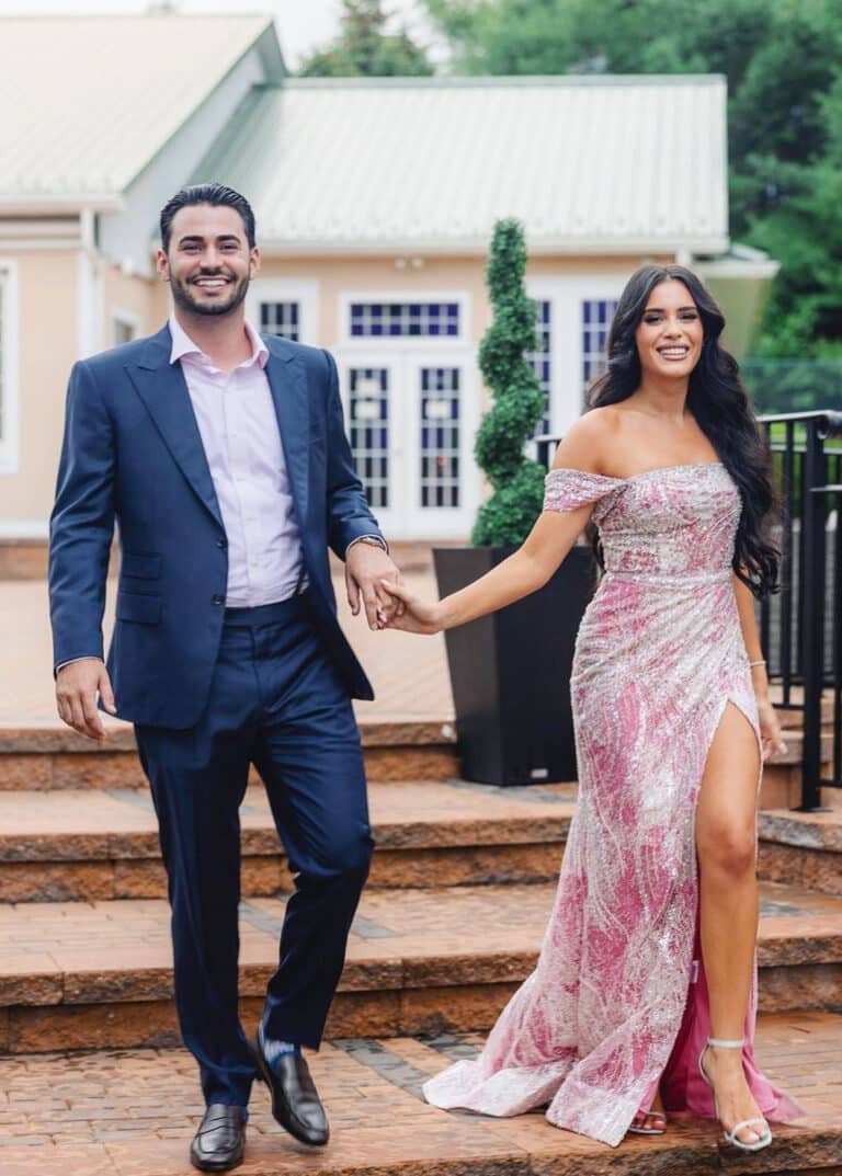 Groomsman and bridesmaid holding hands. Groomsman wearing blue bespoke wedding suit with light blue open collared dress shirt.