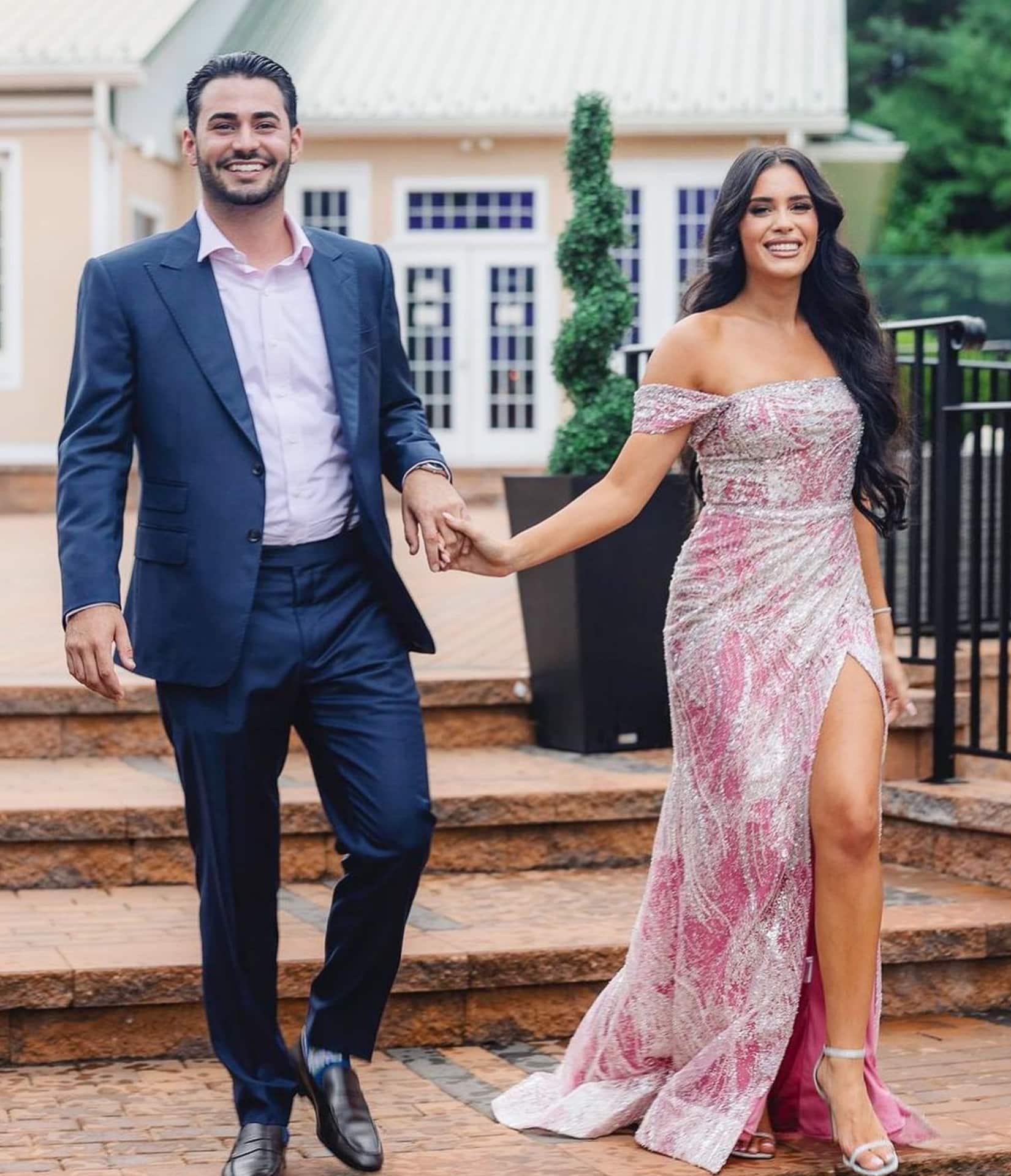 Groomsman and bridesmaid holding hands. Groomsman wearing blue bespoke wedding suit with light blue open collared dress shirt.