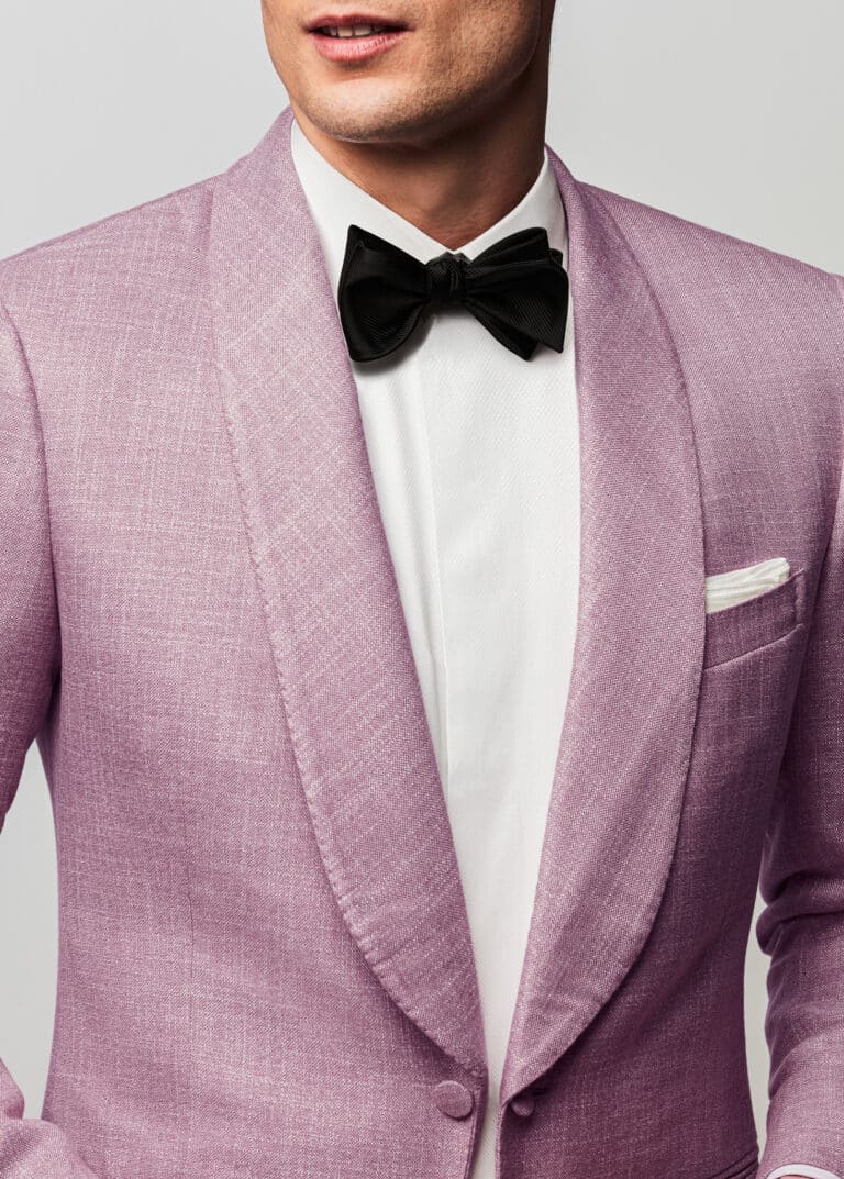Close up of groom in pink bespoke dinner jacket with shawl lapel and a black bowtie.