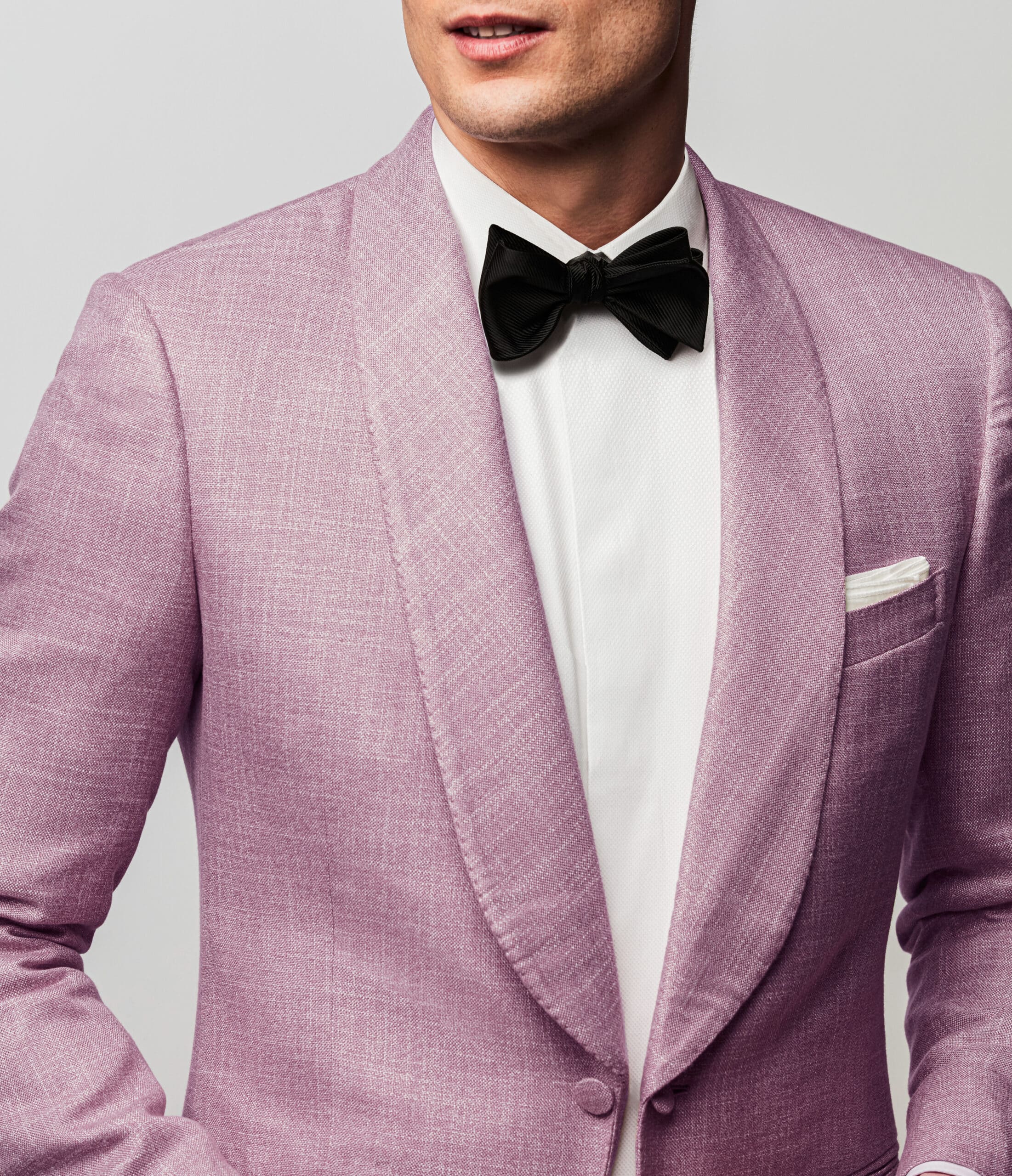 Close up of groom in pink bespoke dinner jacket with shawl lapel and a black bowtie.