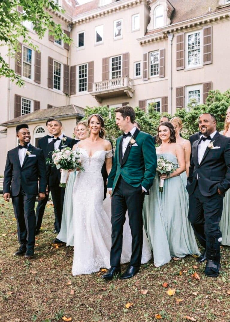 Bride and groom walking with guests. Groom wearing green bespoke wedding dinner jacket with black satin shawl lapel. Bride in wedding dress.