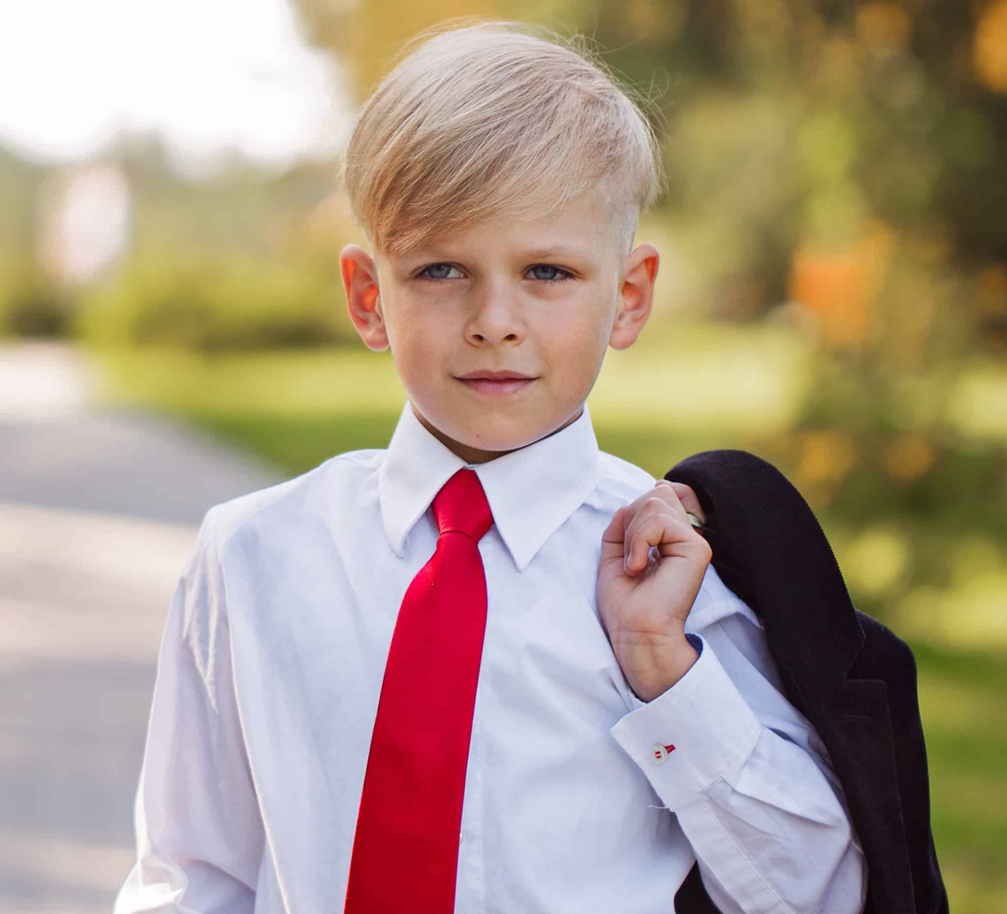Boy with white shirt and red tie and bespoke suit jacket wrapped over his shoulder.