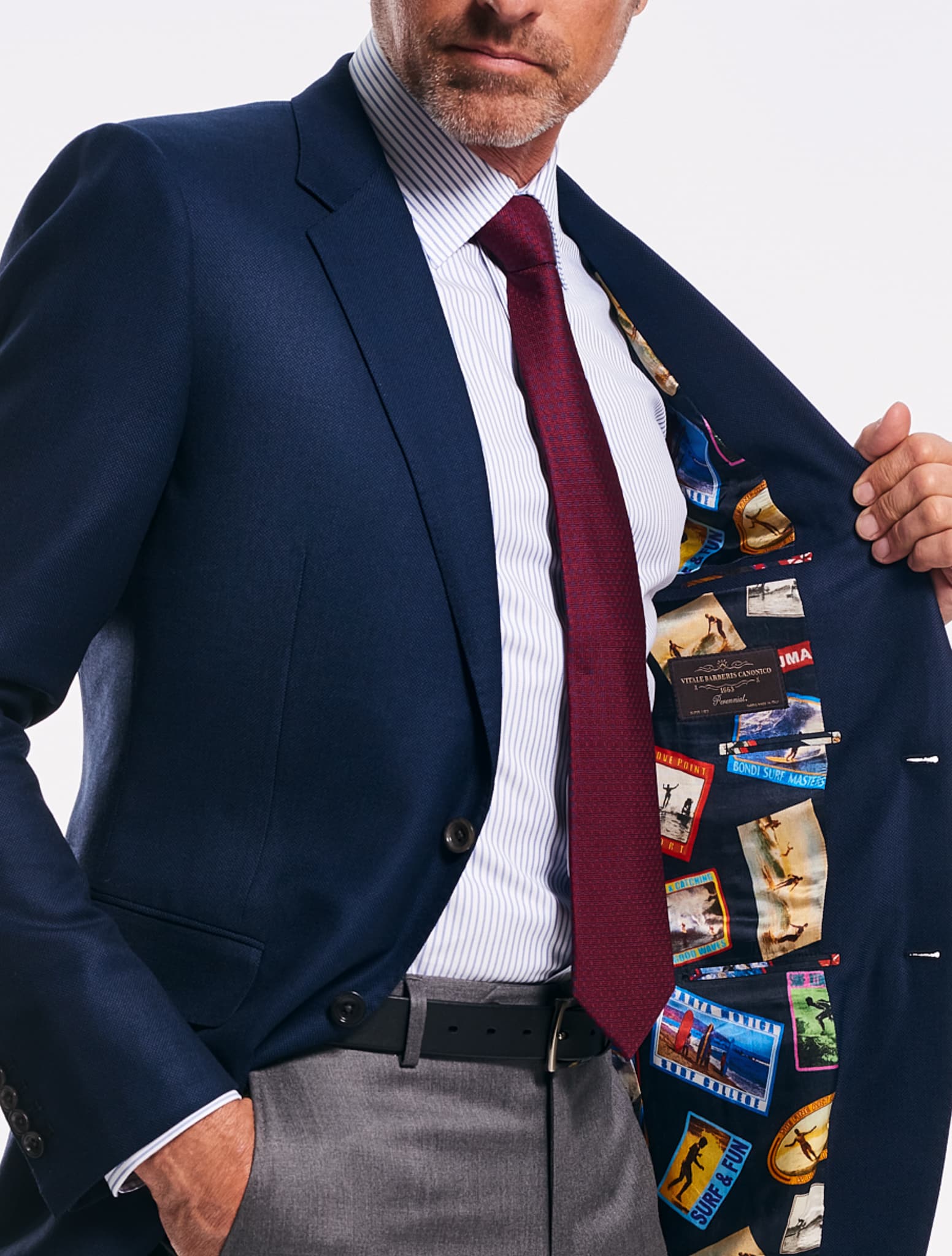 Model wearing classic bespoke navy blazer and medium grey trousers showing off fancy inside lining of multiple vacation destination spots. Fabric by Vitale Barberis.