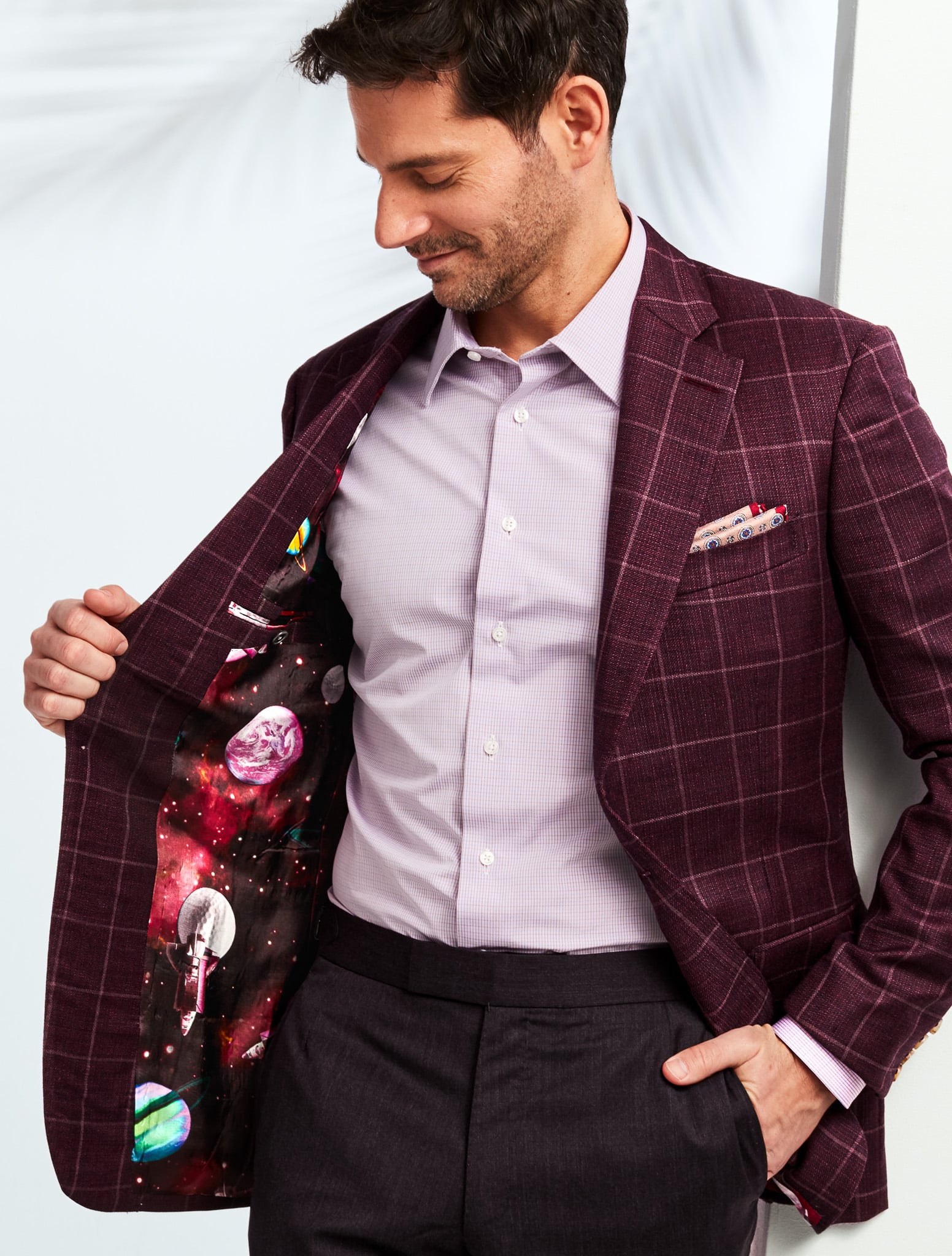 Client wearing a maroon custom tailored sports coat with white windowpane and light blue open collared dress shirt showing off inside fancy lining of outer space.