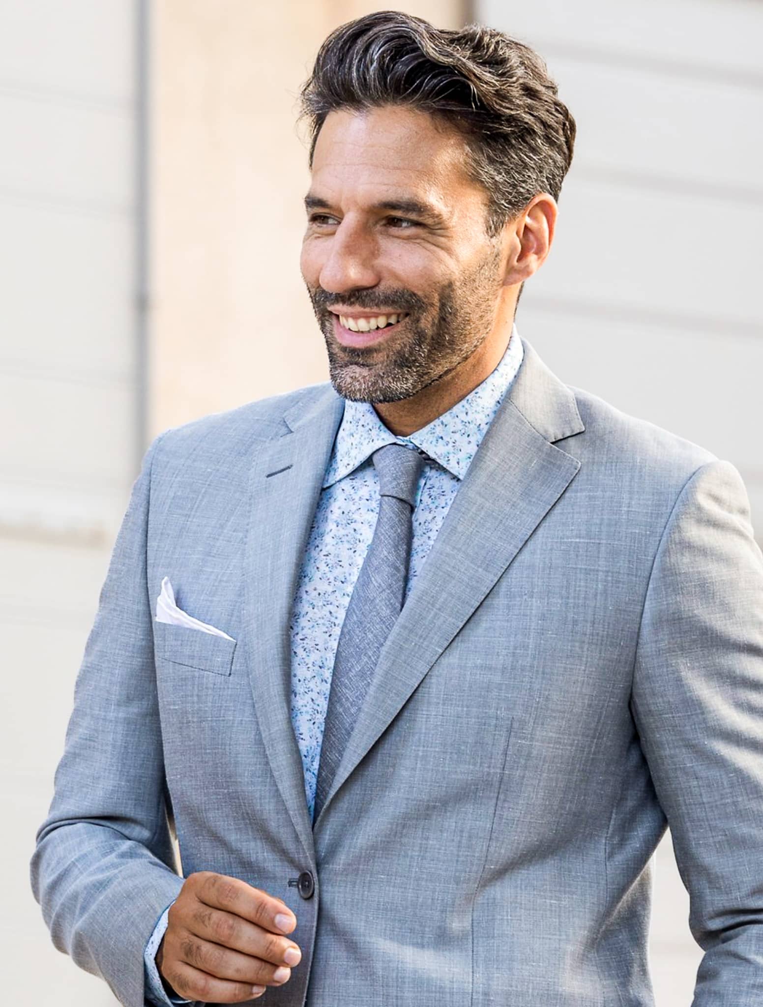 Groomsman wearing light grey custom suit with blue print shirt and blue/grey solid tie.