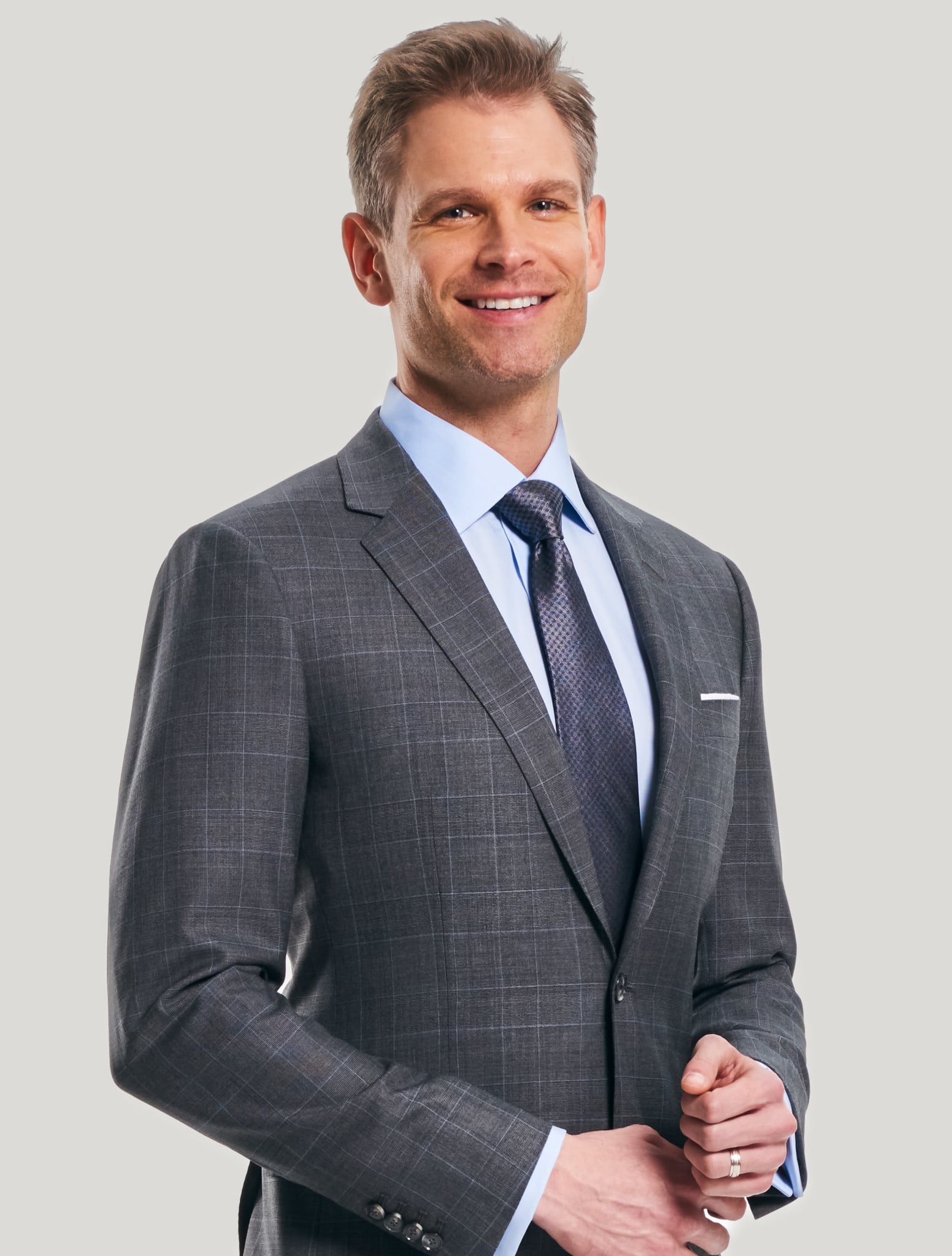 Model wearing grey custom suit with blue plaid and blue shirt with solid grey shiny tie.