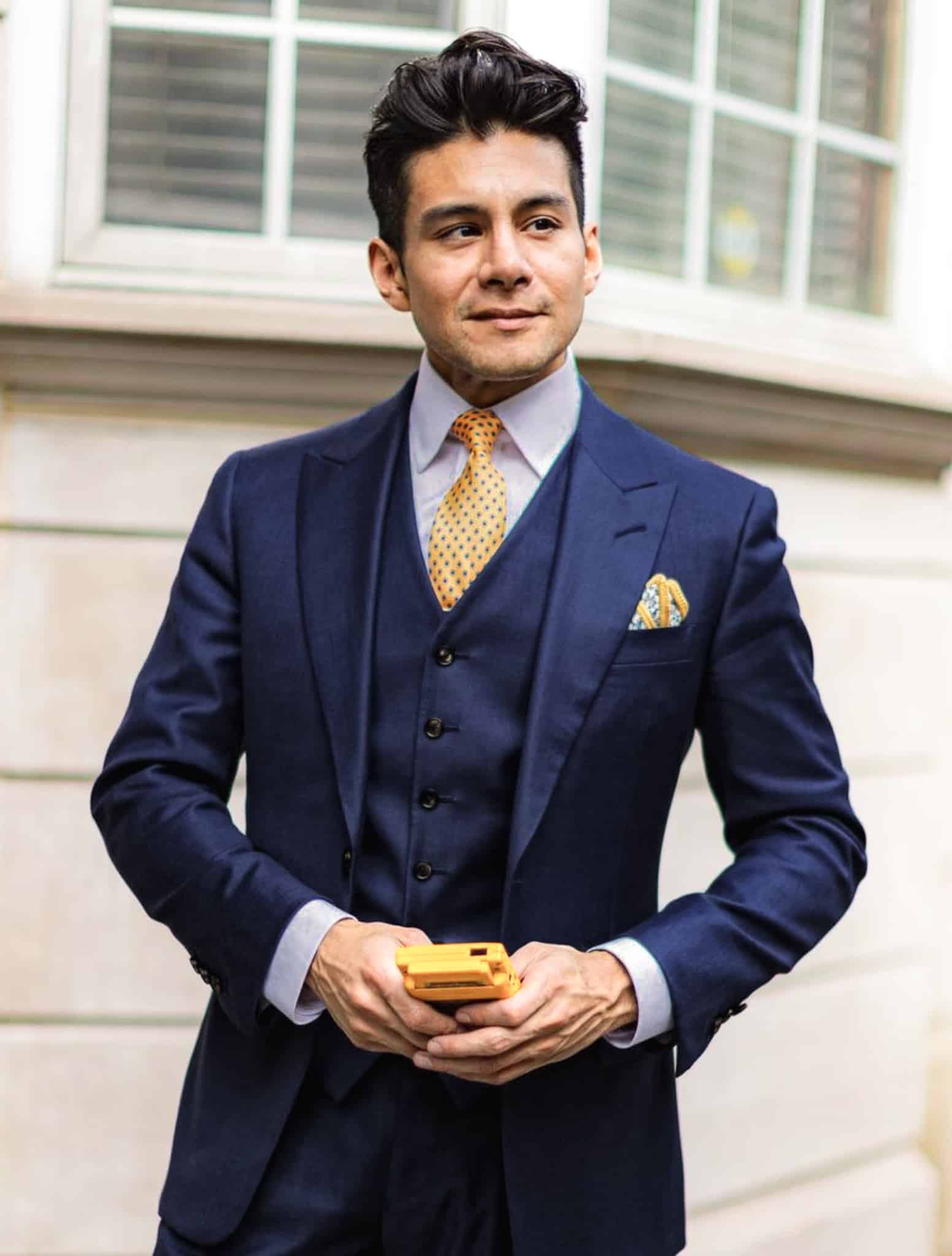 Client in navy blue bespoke three piece suit and white shirt with bright yellow tie. Outdoor picture.