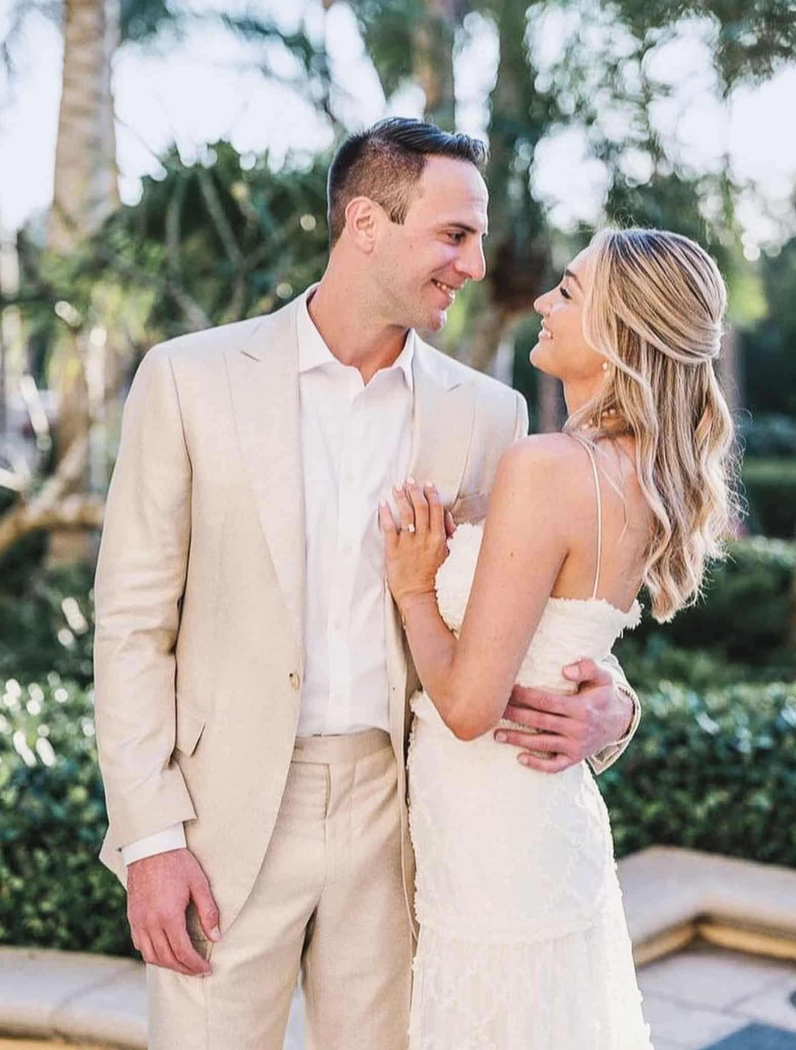 Groom with arm around waist of bride. Groom wearing linen, off white, bespoke suit with open collared white bespoke shirt. Bride in strapless wedding dress.