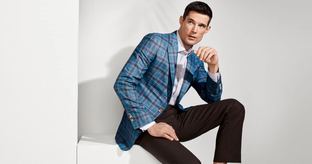 Model wearing light blue with navy big plaid custom tailored sportscoat with white shirt and navy trousers.