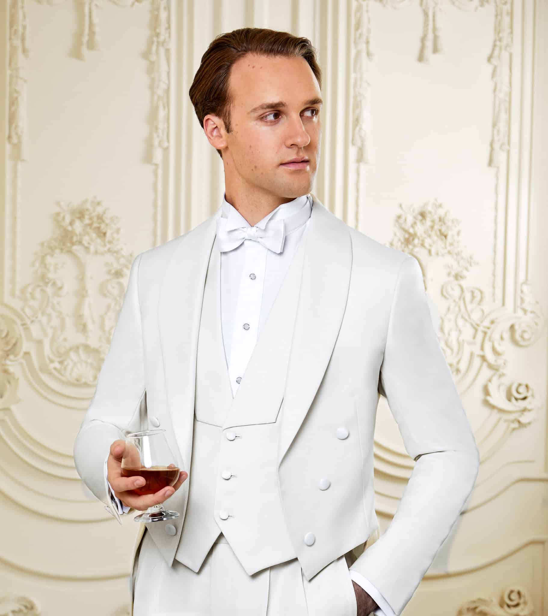 Client in white vested full dress bespoke tails for wedding. Vest has shawl lapel. White shirt and bowtie. Fabric by Loro Piana.