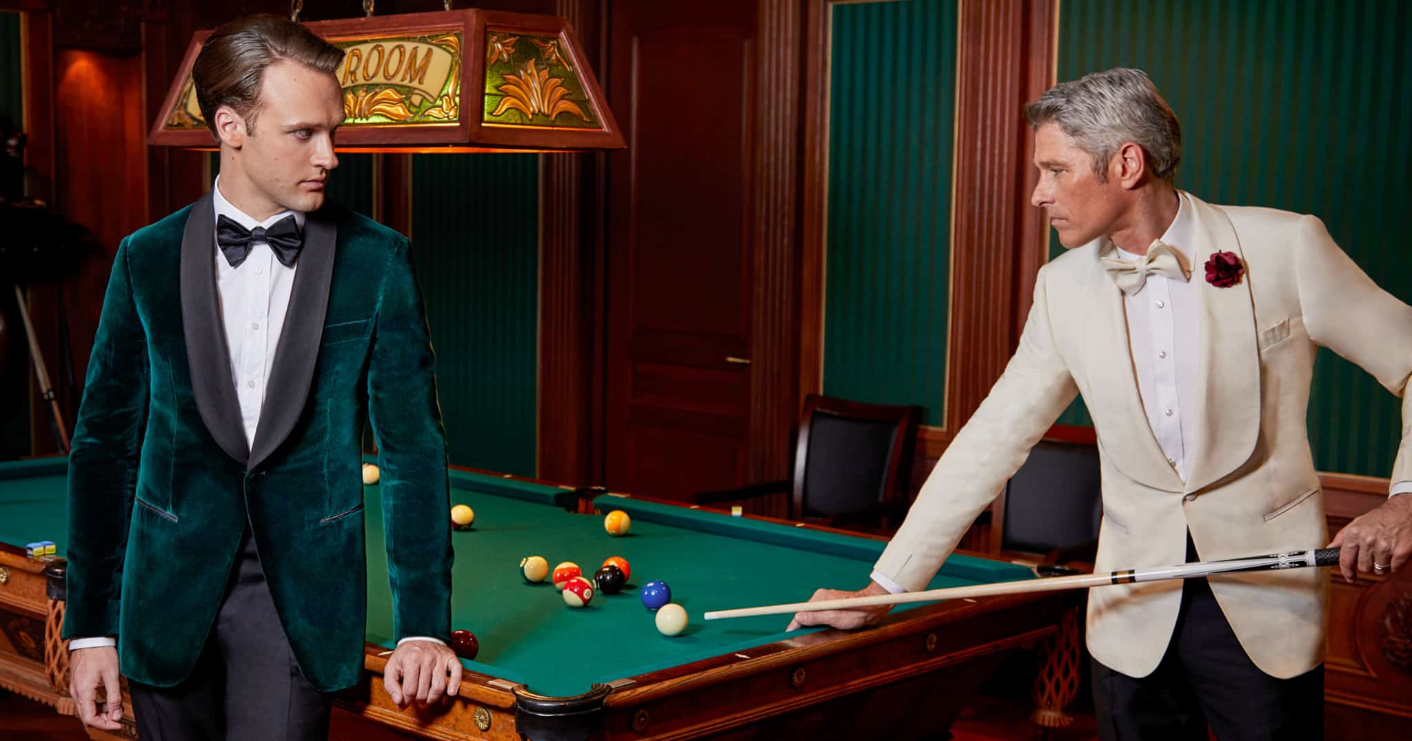 Two models shooting pool. One in green bespoke tuxedo wedding jacket with black lapel. One with white bespoke tuxedo jacket with wide shawl lapel.