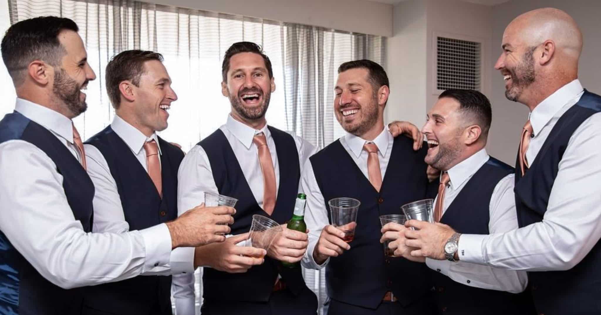 Six groomsmen in navy custom made vests, white dress shirts and solid orange ties.