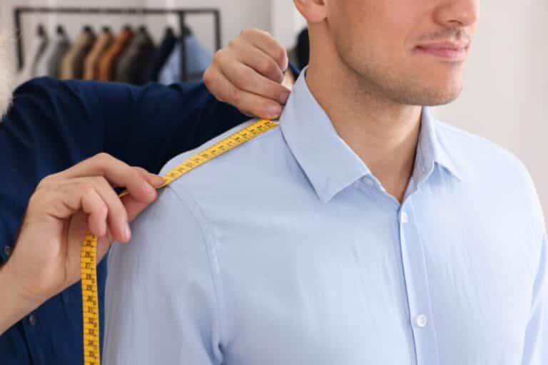 Professional tailor measuring shoulder seam length on client's shirt in atelier, closeup