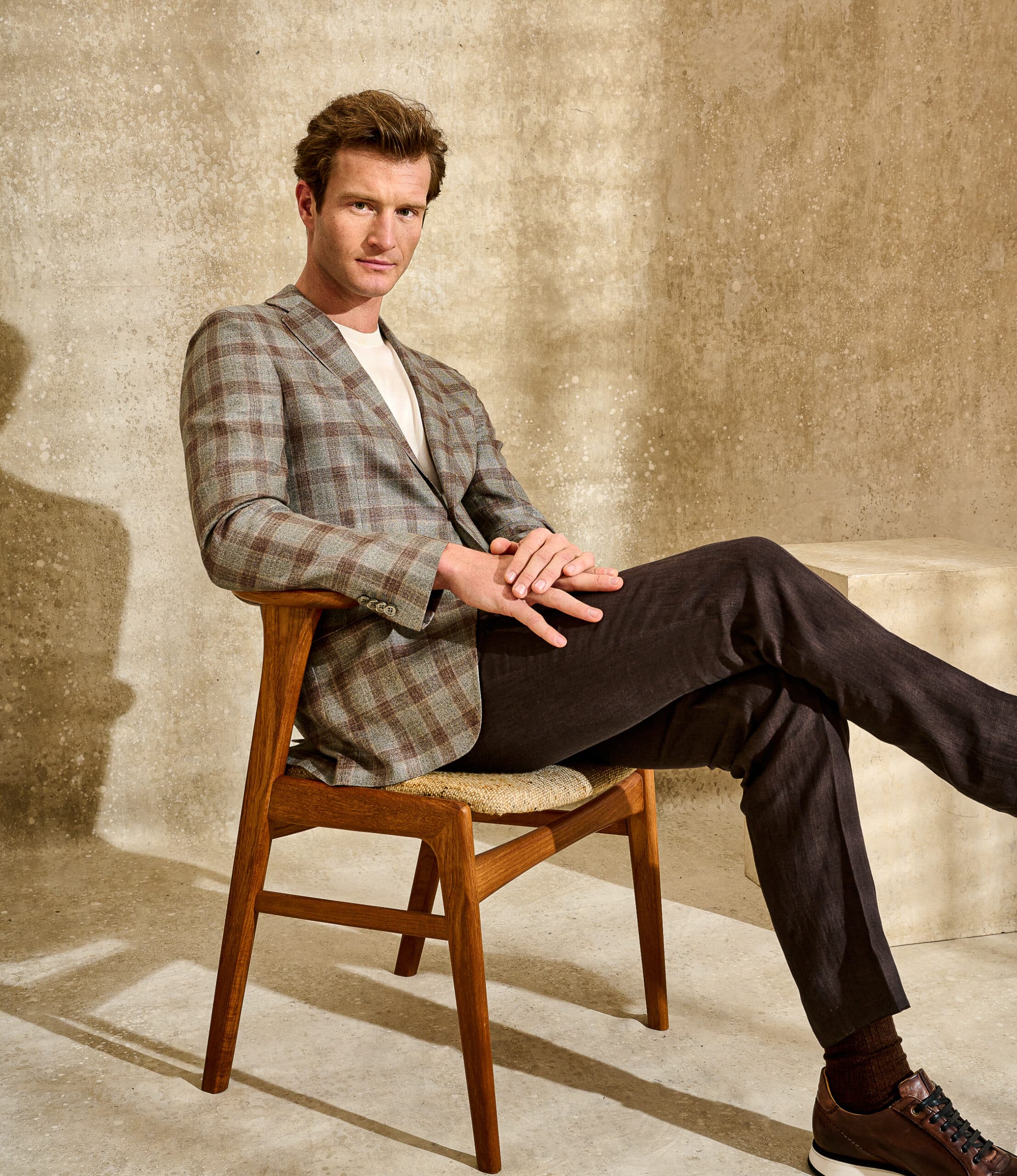 Model sitting wearing Scabal bespoke light brown sportcoat with dark brown plaid, solid brown twill trousers