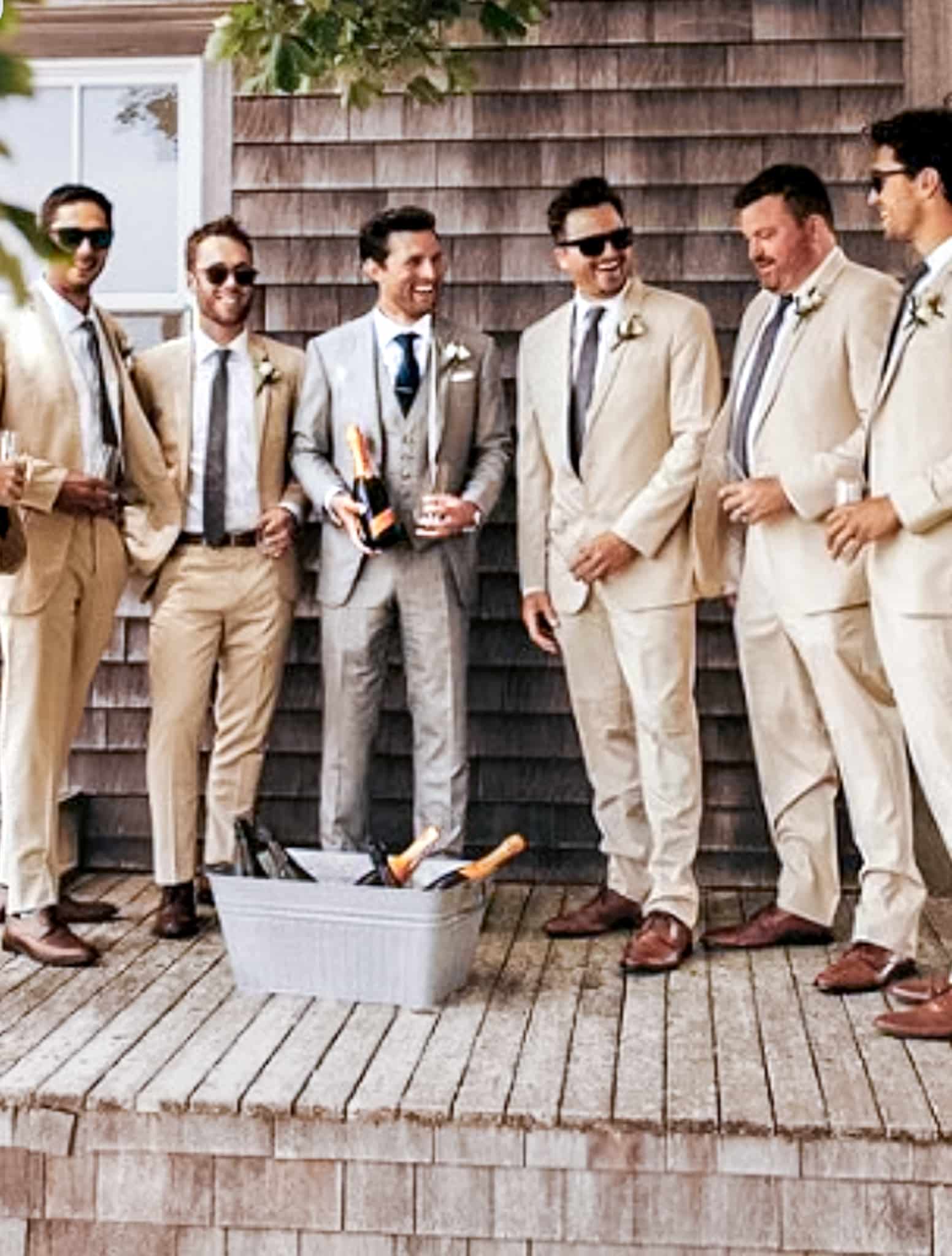 Six groomsmen all wearing tan colored custom suits talking with each other.
