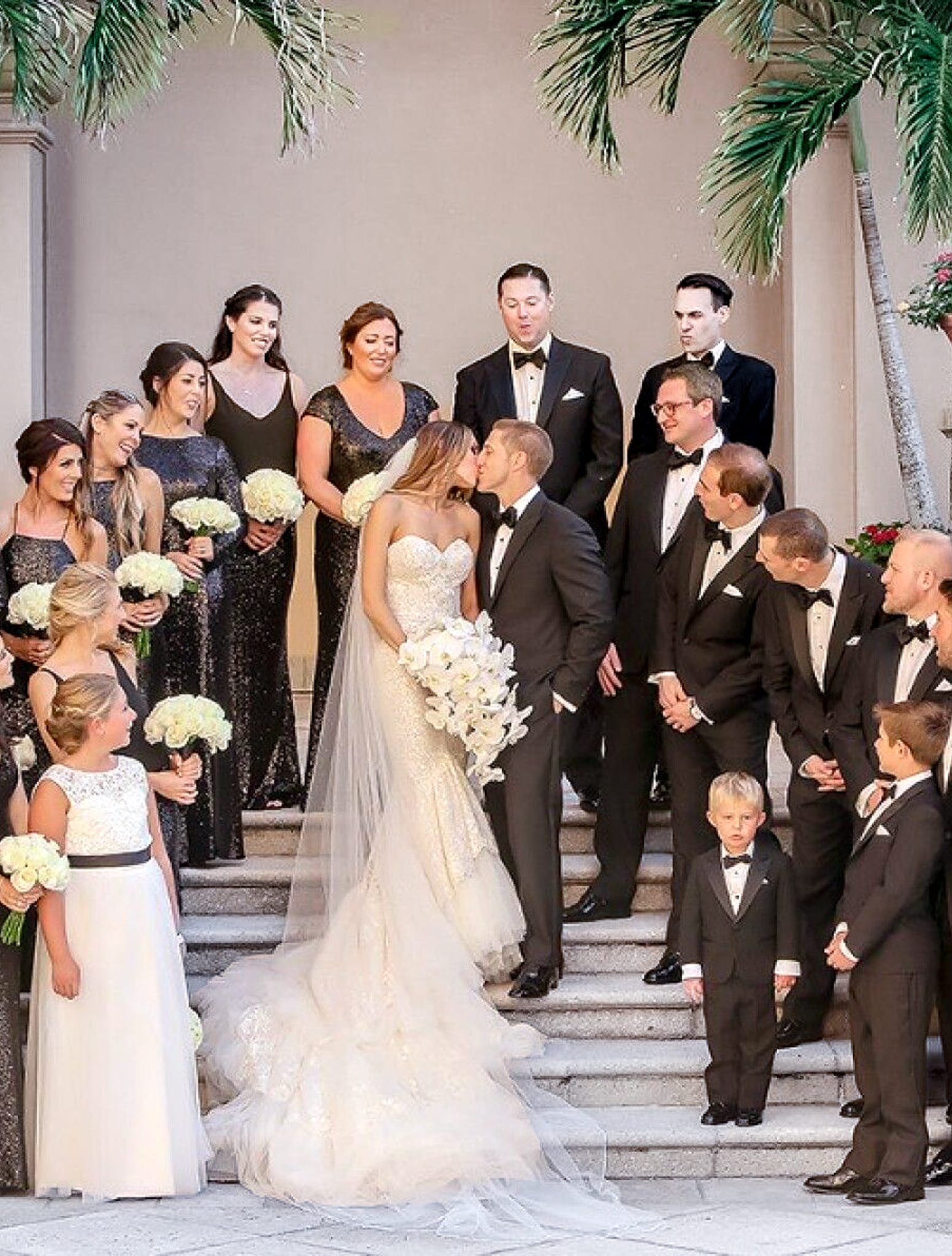 Bride and groom kissing in middle of their grooms and bridesmaids. Groom in black bespoke wedding tuxedo.