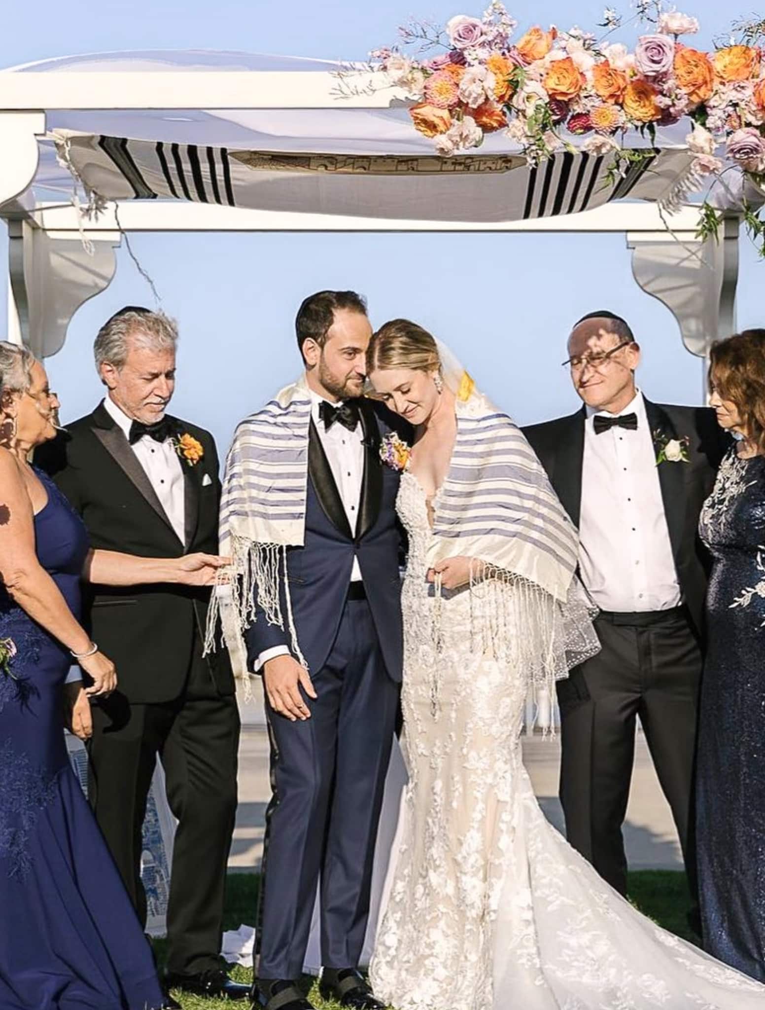 Bride and groom and sets of parents under Chupah. Bride and groom wearing a Talis. Groom in navy bespoke suit.