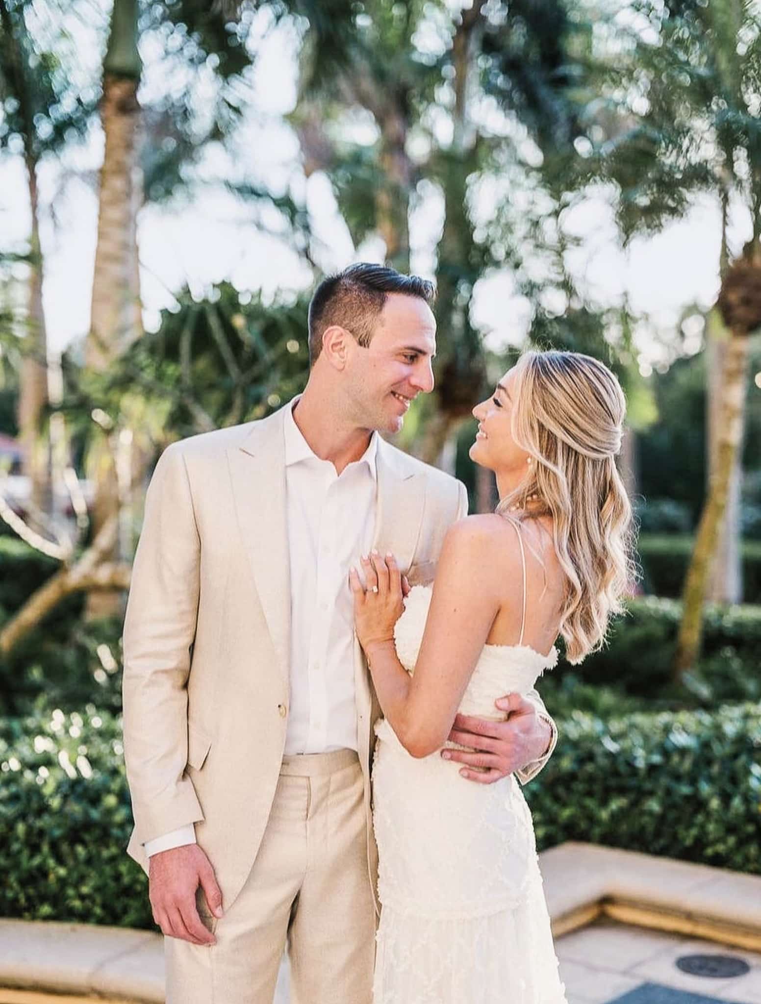 Groom and bride on beach looking at each other. Groom in off white custom made linen suit, bride in wedding dress.