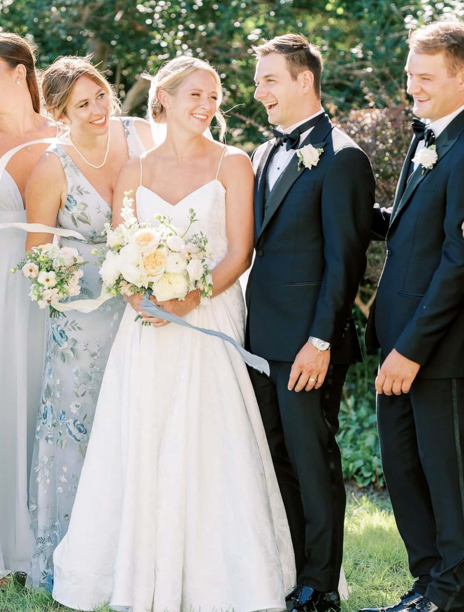 Two ushers and two bridesmaids talking. Groomsmen wearing black custom made wedding tuxedos with white shirts and black bowties.