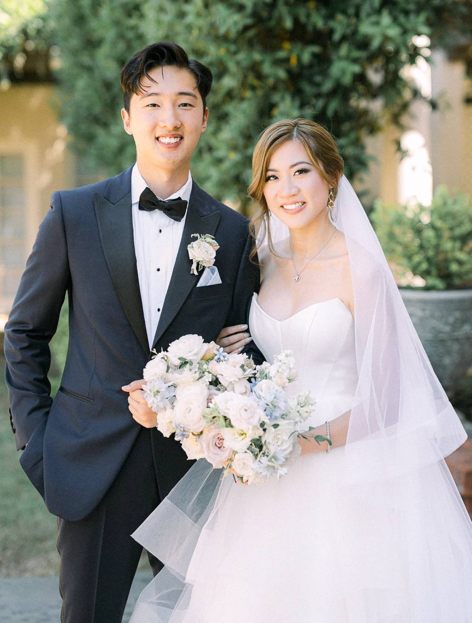 Bride & groom outdoors. Groom wearing midnight navy Scabal wedding tuxedo with white shirt and black bowtie. Bride in low cut wedding dress.