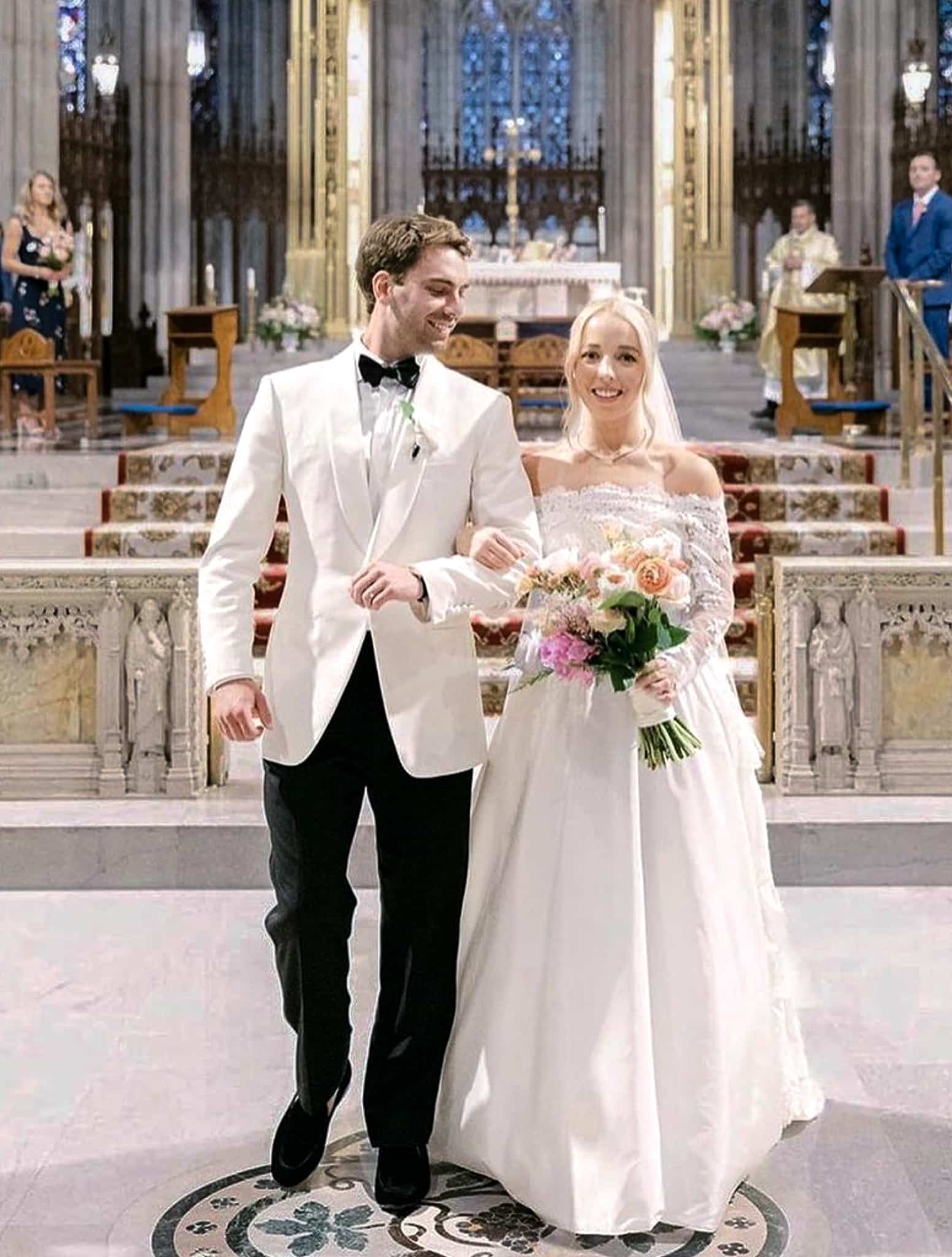 Bride and groom with cross in background. Groom wearing Loro Piana custom made white dinner jacket with black trousers, white shirt and black bowtie. Bride in classic white dress.