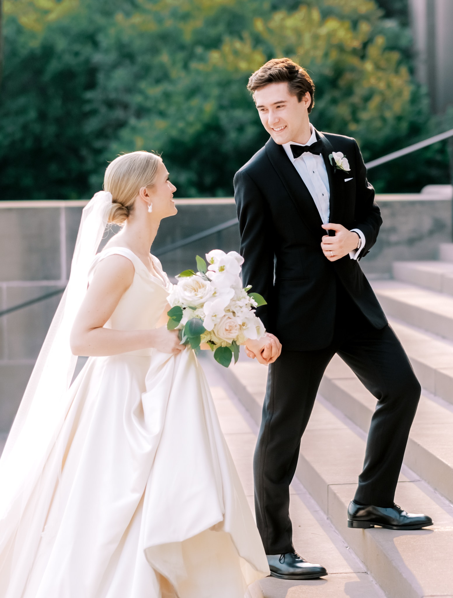 Groom helping bride up steps. Groom wearing Vitale Barberis black custom made tuxedo. Bride in sleeveless wedding gown.