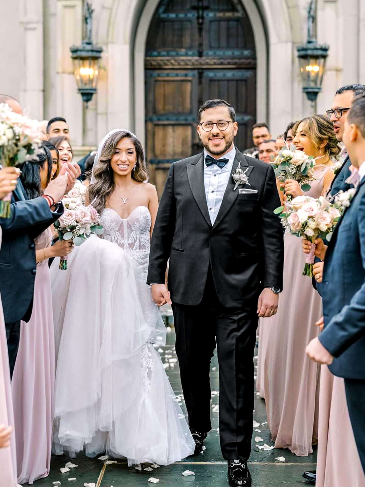 Bride and groom leaving Church. Groom in classic black custom wedding tuxedo with white shirt and black bowtie. Fabric by Vitale Barberis. Bride in classic wedding dress.