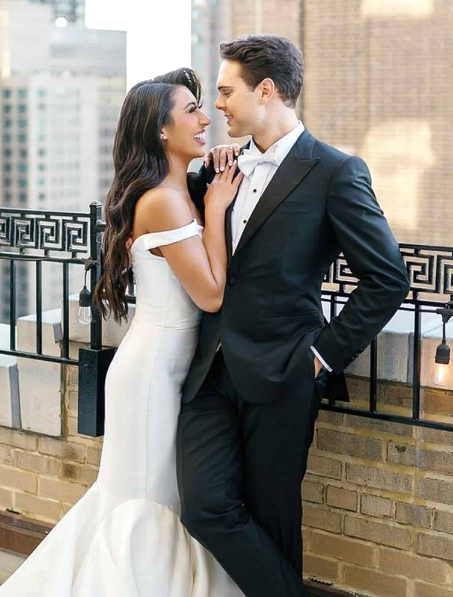Groom getting close with bride in his dark navy custom wedding tuxedo with custom white shirt and white bowtie. Bride in skimpy wedding dress.