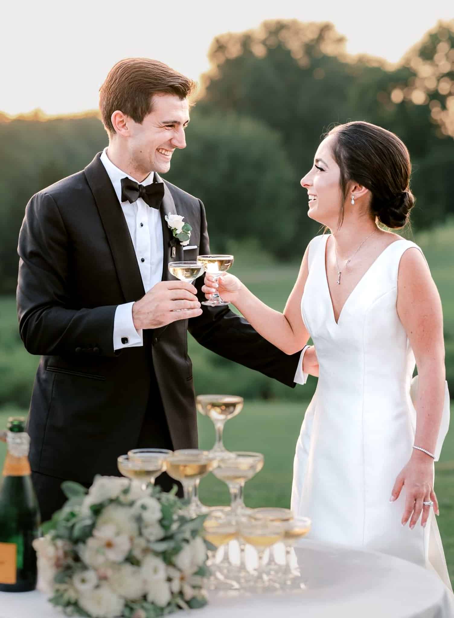 Bride and groom toasting. Groom wearing Zegna black classic Drago wedding tuxedo with white shirt and black bowtie. Bride in casual sleeveless wedding dress.