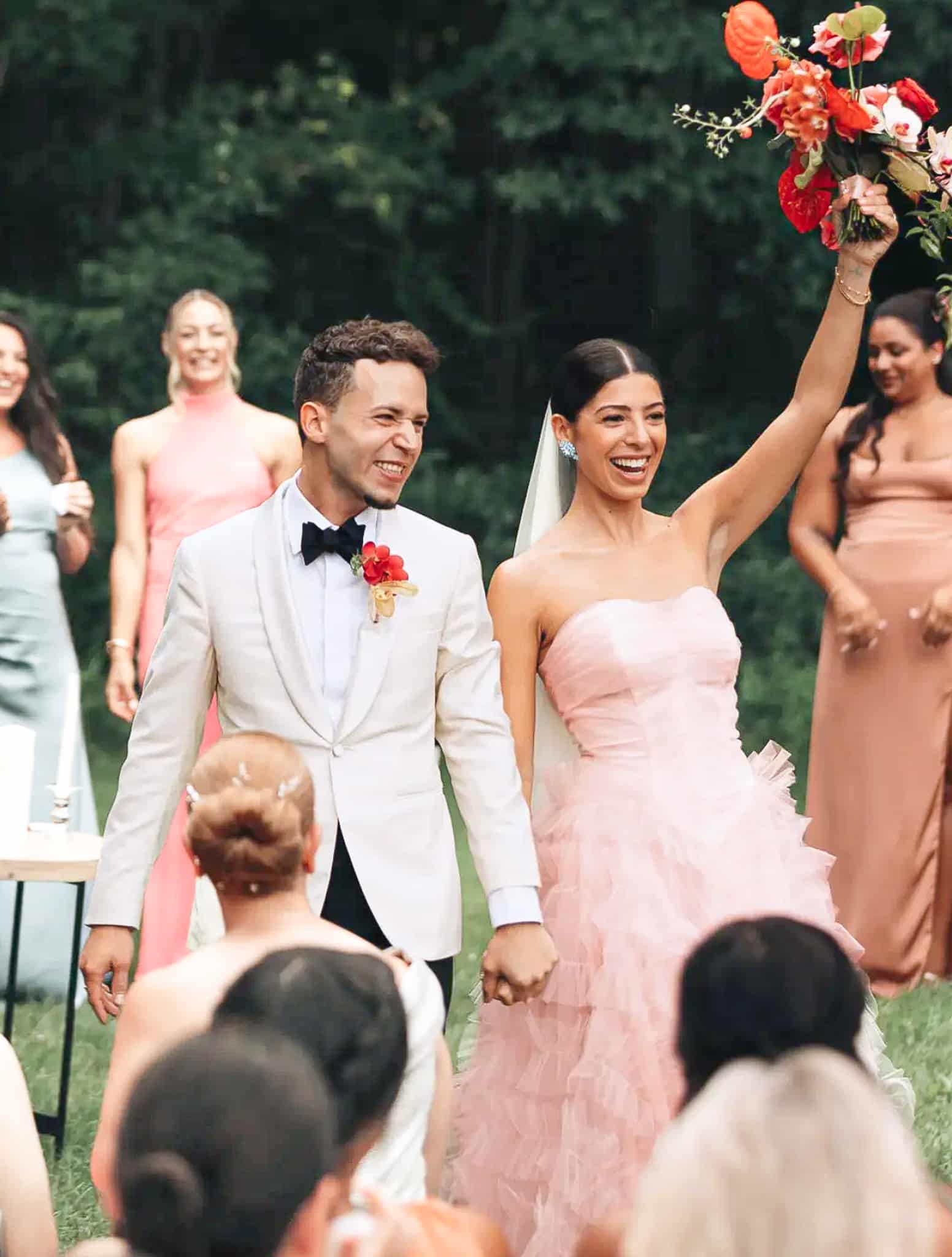 Groom holding brides hand wearing white custom tailored Zegna dinner jacket and black trousers with white shirt and black bowtie.
