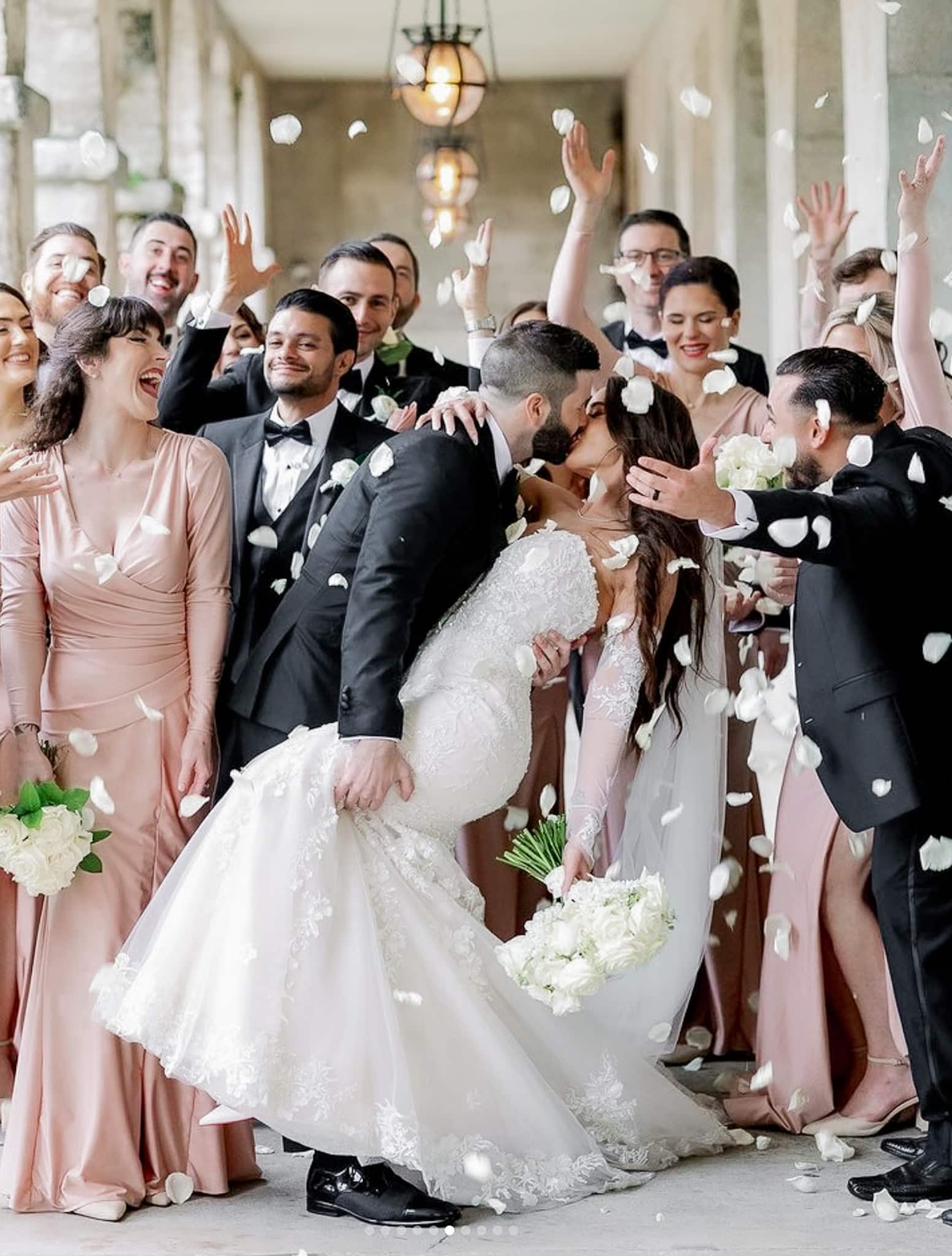 Groom kissing bride in middle of their wedding party guests. Groom wearing bespoke wedding tuxedo, bride in classic wedding dress.