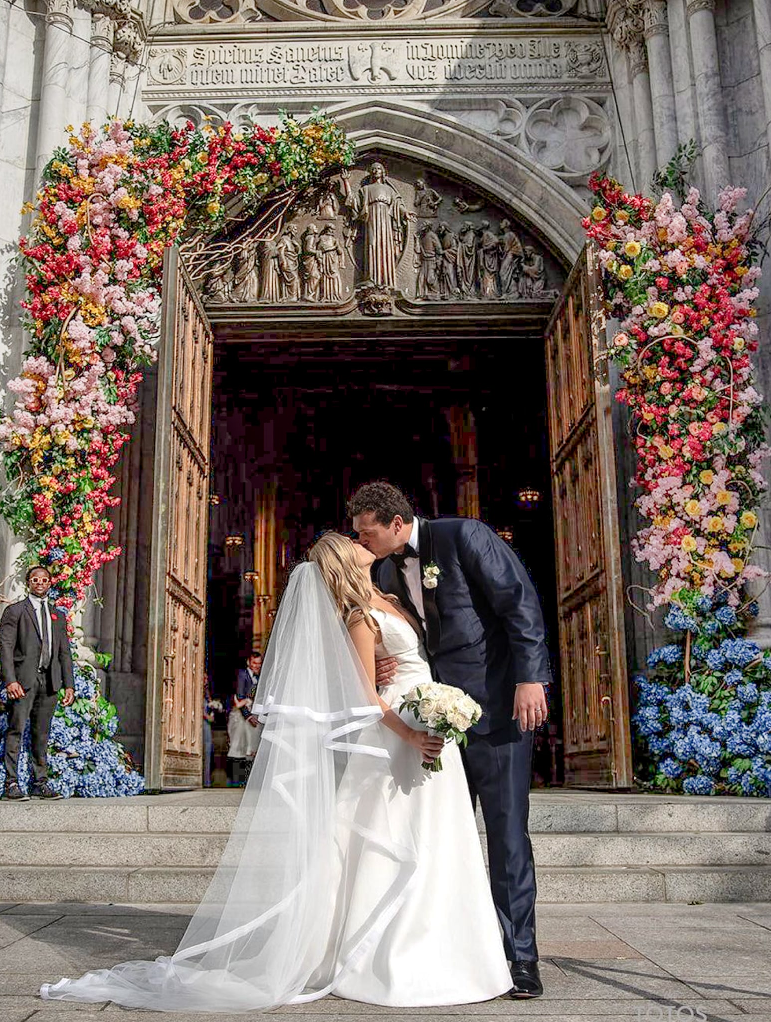 Bride and groom kissing outside Hungarian church. Groom wearing navy Scabal wedding tuxedo, bride in wedding gown.