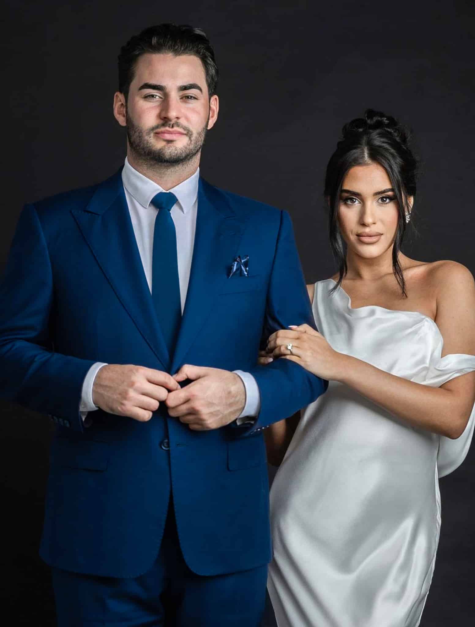 Bride and groom arm in arm. Groom in blue wedding suit with white shirt and long blue tie. Bride in off the shoulder wedding dress.