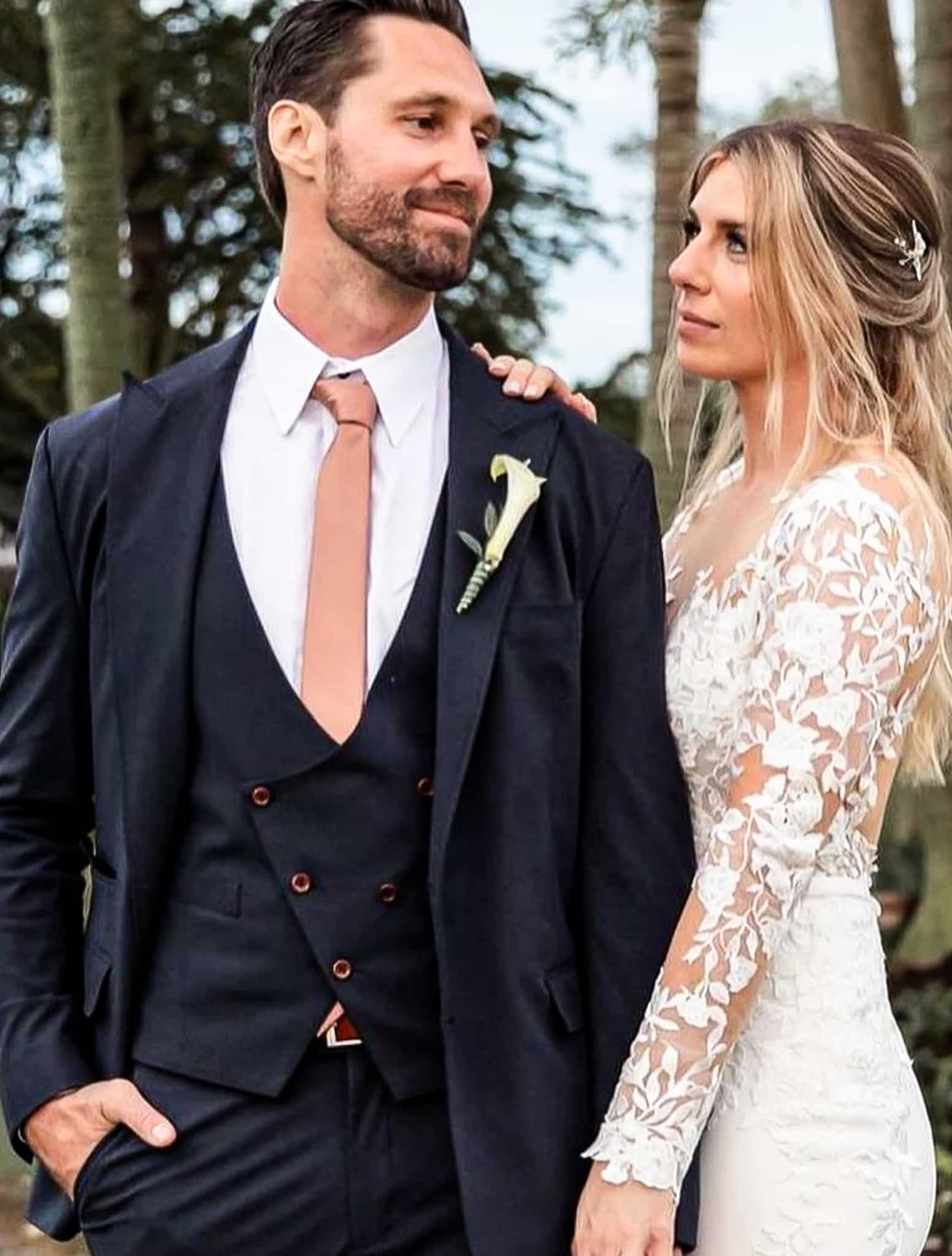 Bride and groom looking at each other. Groom wearing navy custom tailored wedding suit with navy double breasted six on three u shaped vest, white dress shirt and beige long tie. Bride in classic casual wedding dress.