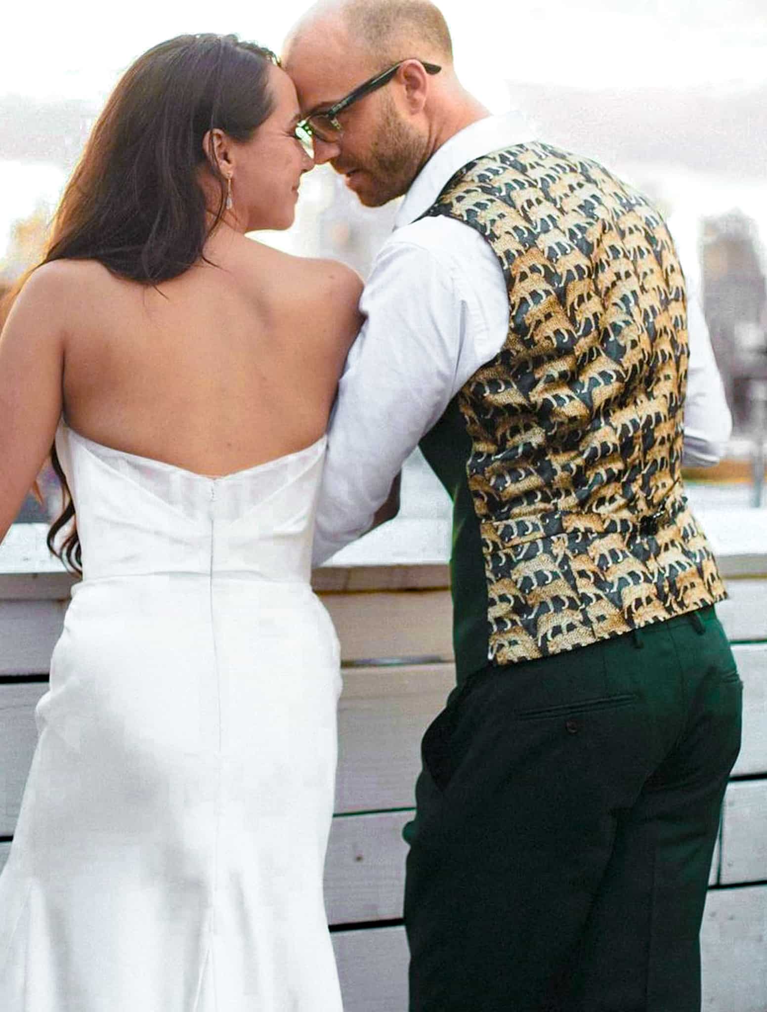 Bride and groom looking over a ledge. Groom wearing bespoke wedding vest showing off brown and blue fancy pattern on back of vest.