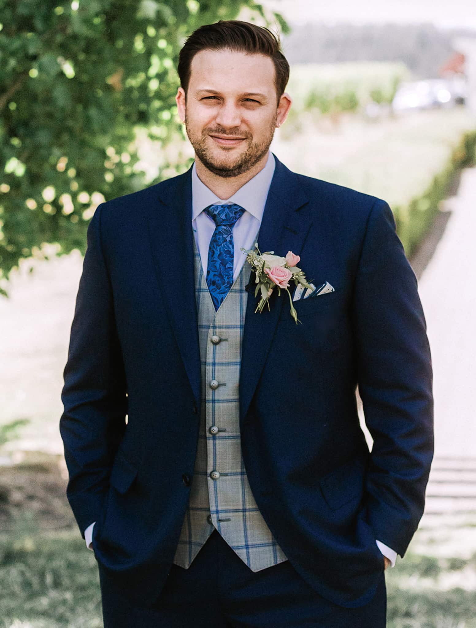 Groomsman wearing navy blue bespoke suit with light grey vest and blue windowpane on vest, white shirt and long blue paisley tie. Ermenegildo Zegna fabric for suit.
